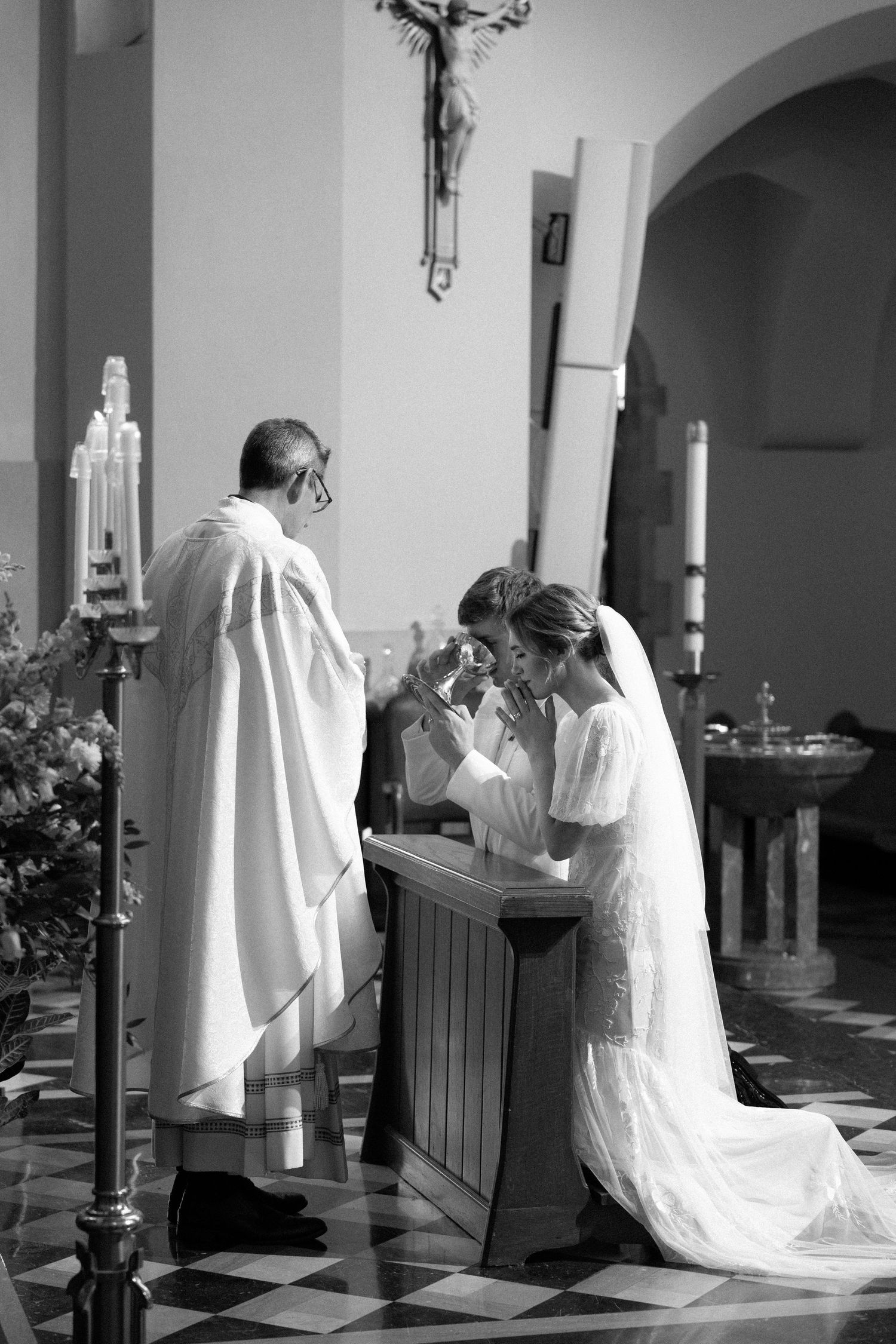 Black and white photo of a Catholic wedding ceremony taking place at the altar with a priest in white robes.