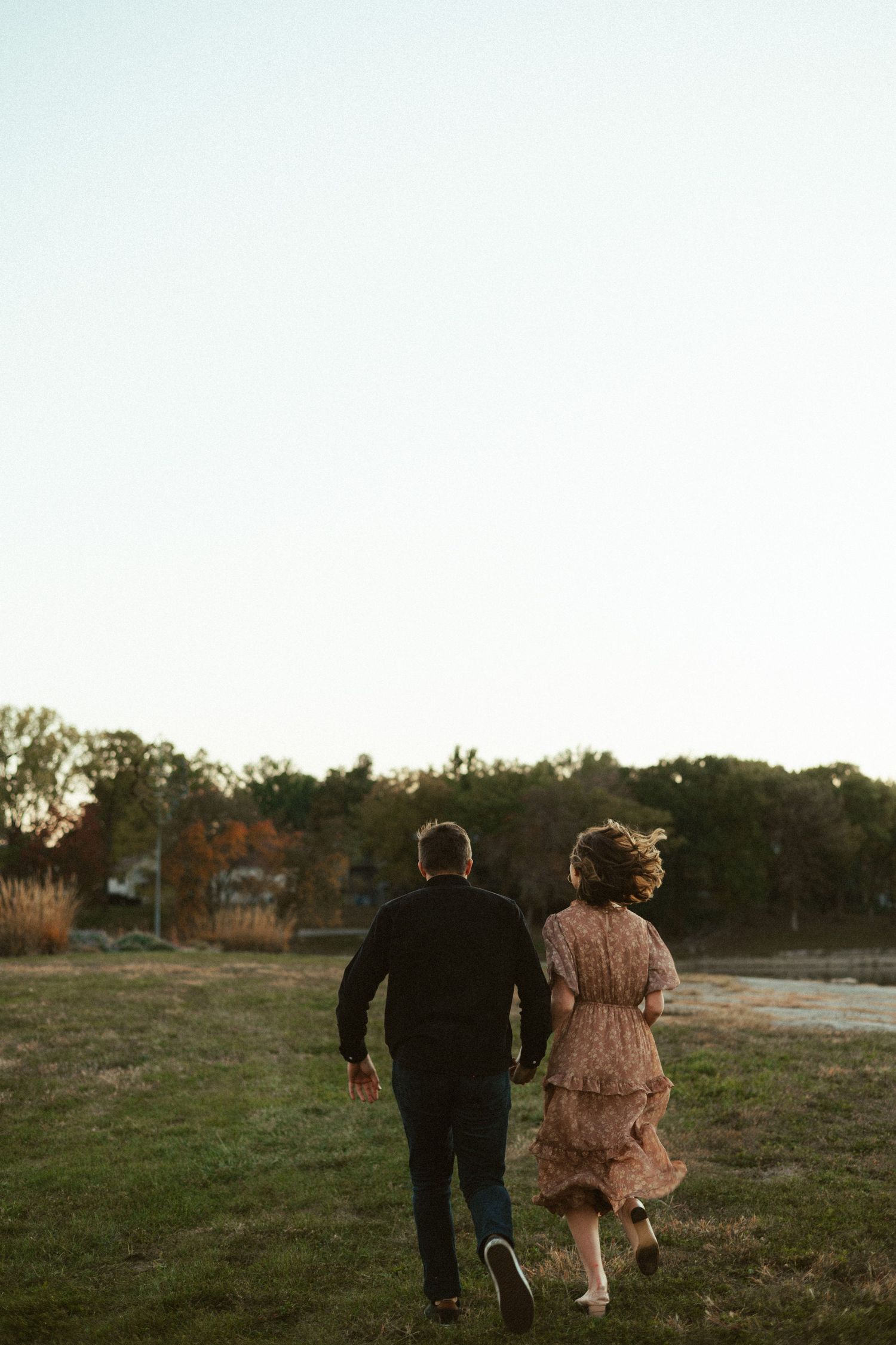 A couple walking together across an open field at sunset.