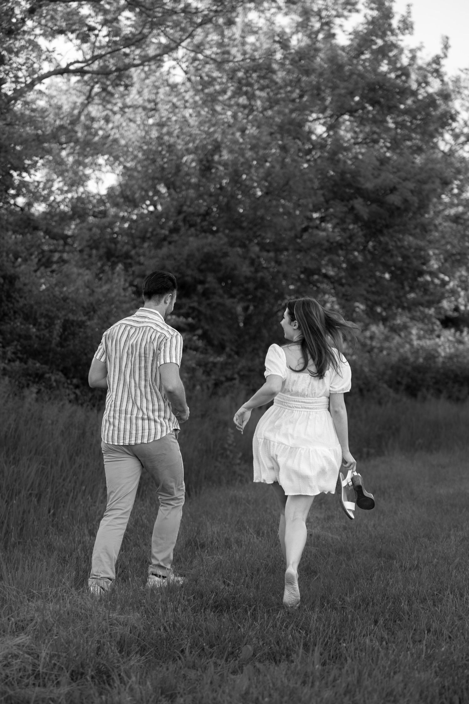 Black and white photo of couple running playfully through tall grass.