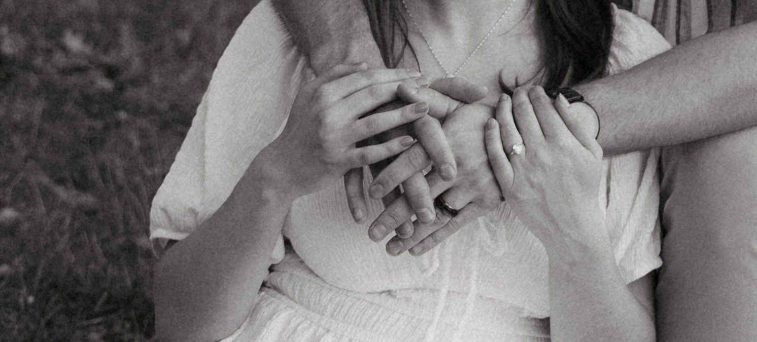 Black and white close-up of hands clasped together showing wedding rings.