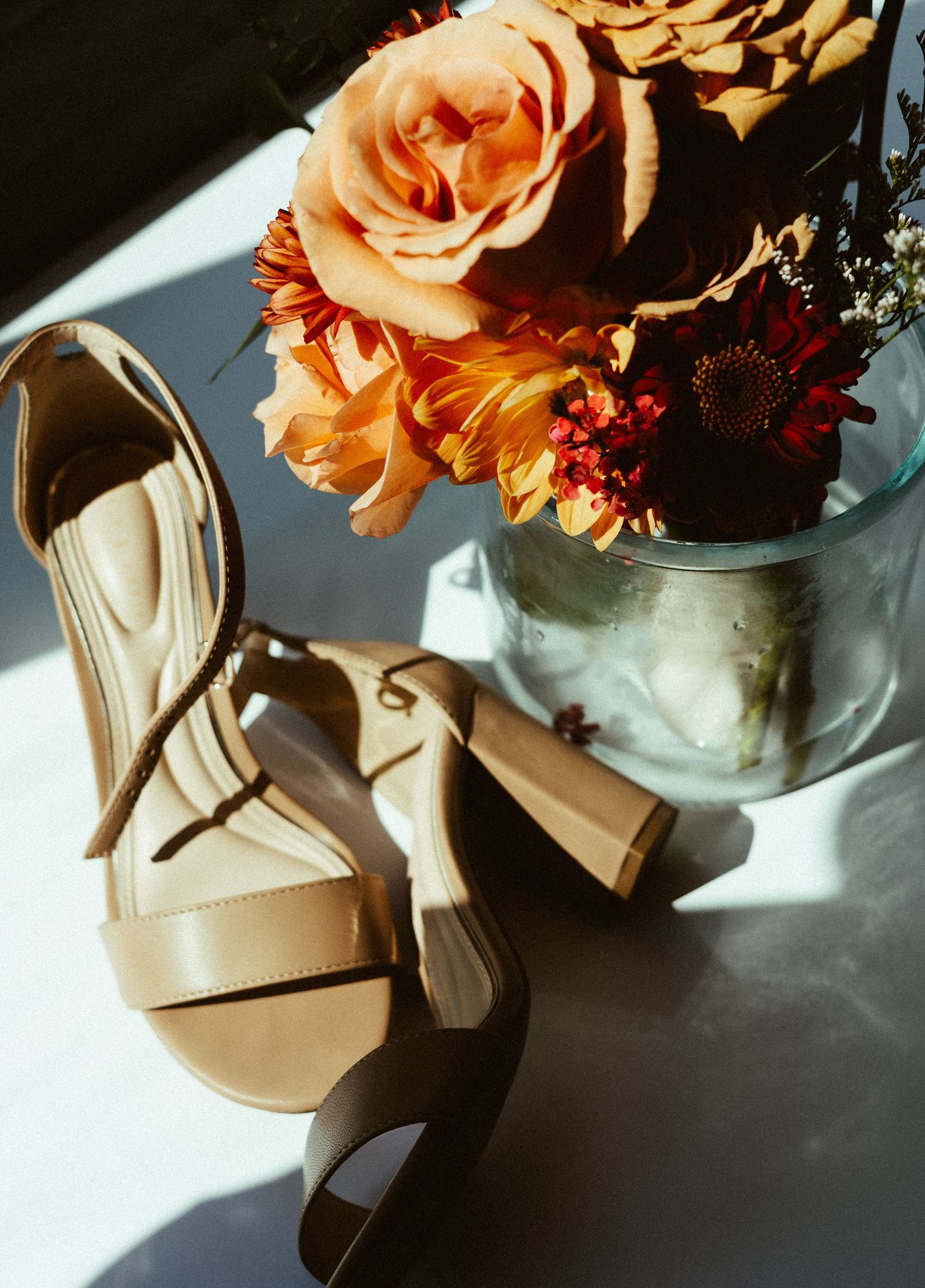 Peach roses and burgundy flowers arranged with bridal shoes in dramatic lighting.