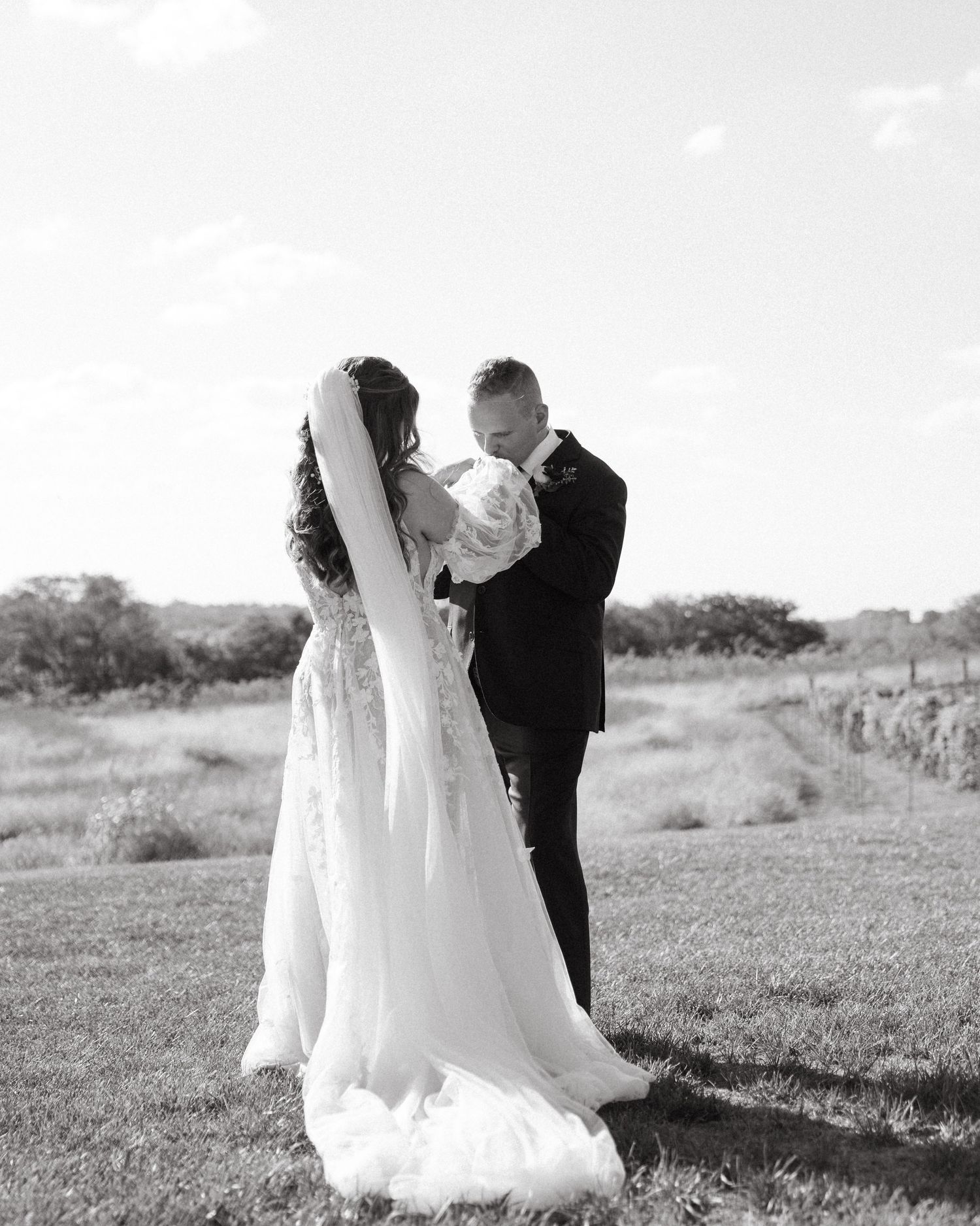 Black and white photo of newlyweds embracing in outdoor setting with flowing wedding dress.