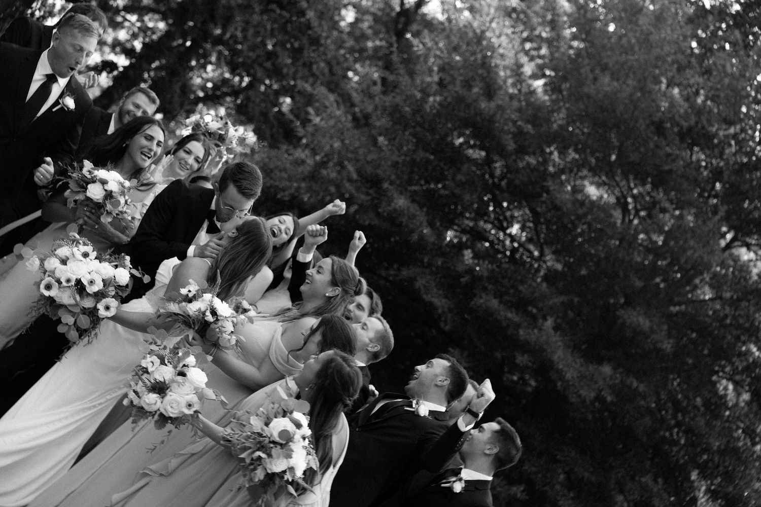 A black and white wedding party photo showing bridesmaids in matching dresses holding bouquets outdoors.