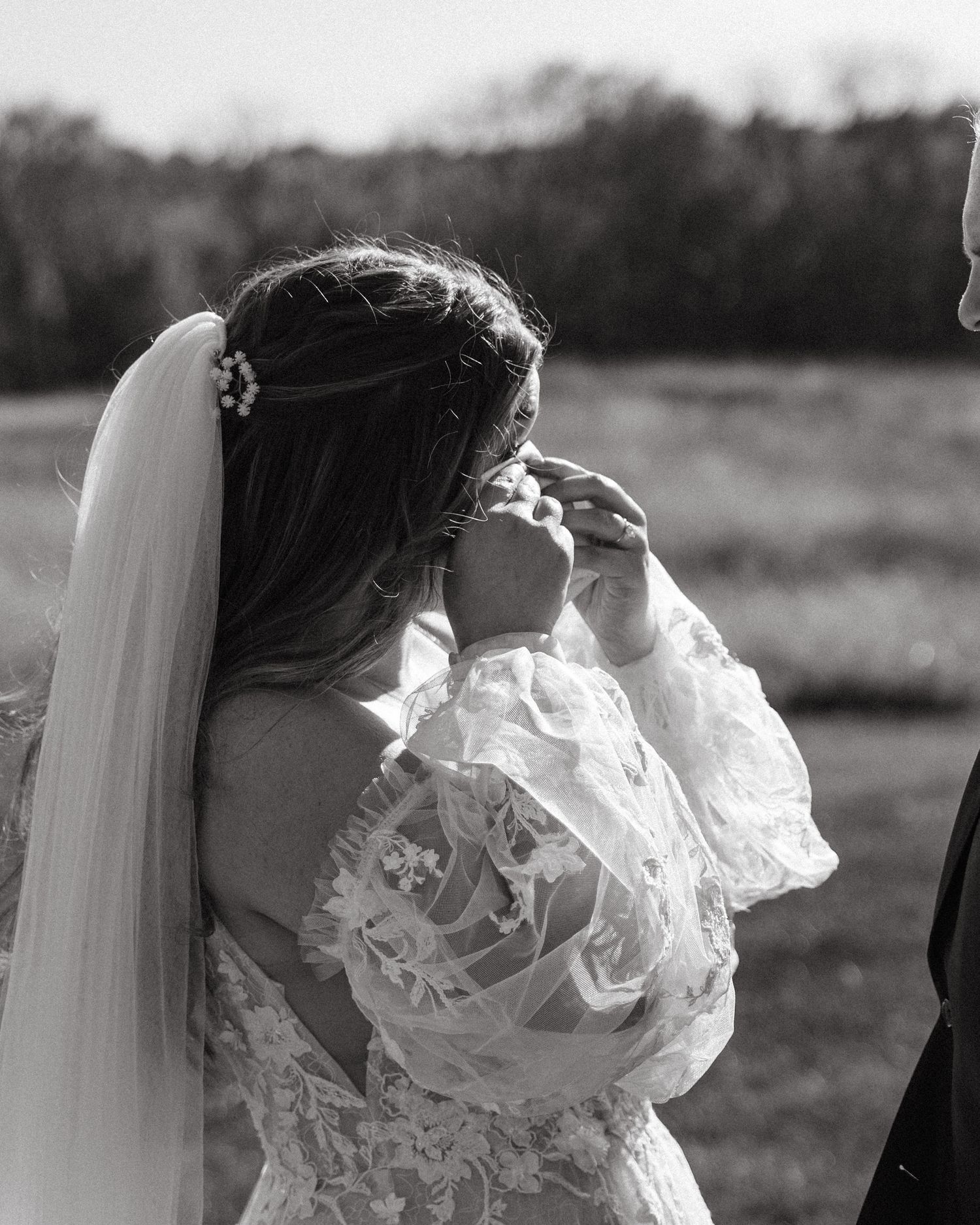 A romantic black and white photo of a couple embracing in delicate lace wedding attire.