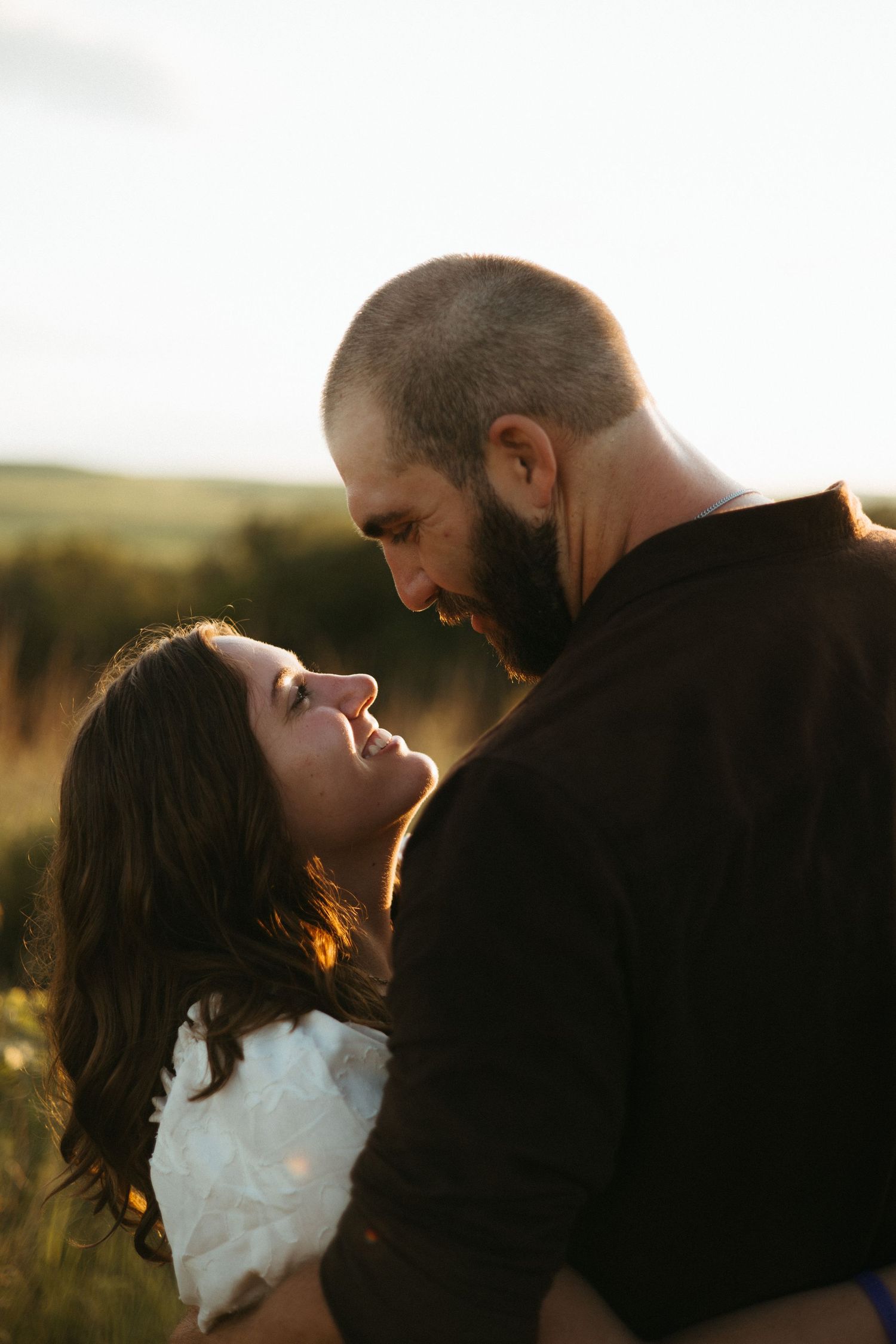 A couple shares an intimate moment at sunset in a golden field with warm backlighting creating a romantic silhouette.
