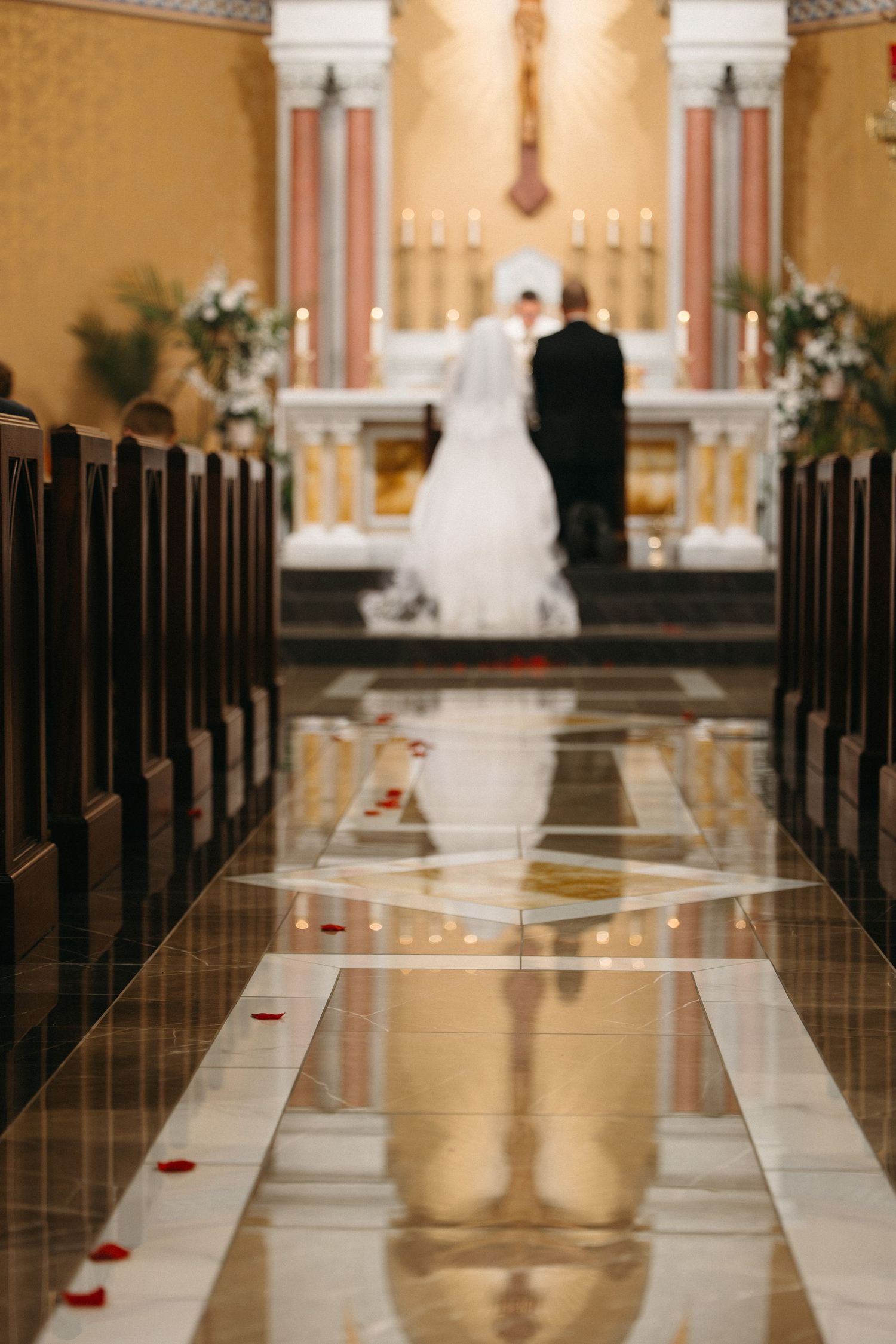 A wedding ceremony aisle in an elegant church with dark wooden pews and red accents along the marble floor.