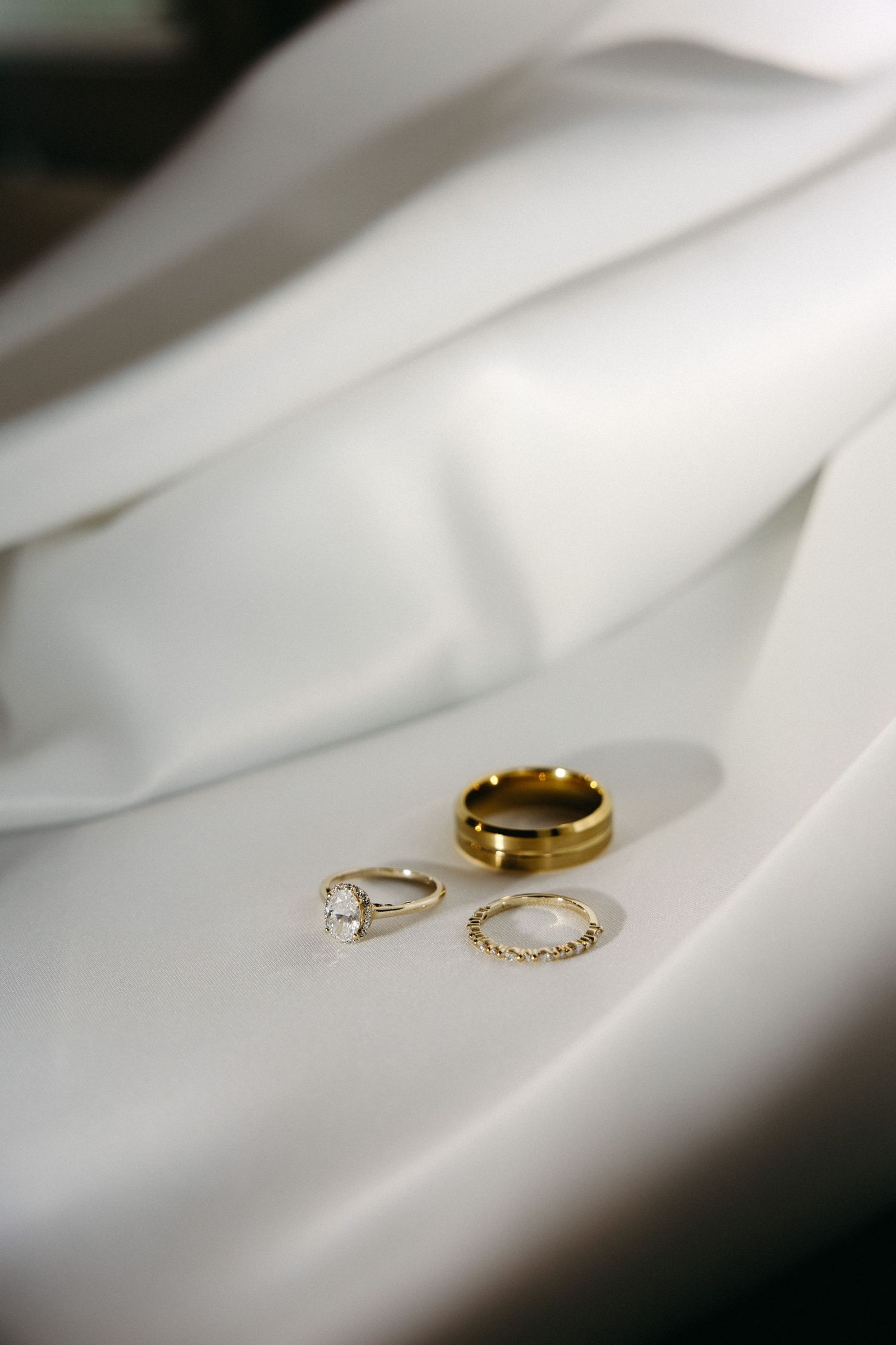 Three elegant wedding rings including a diamond engagement ring and gold bands rest on white silk fabric.