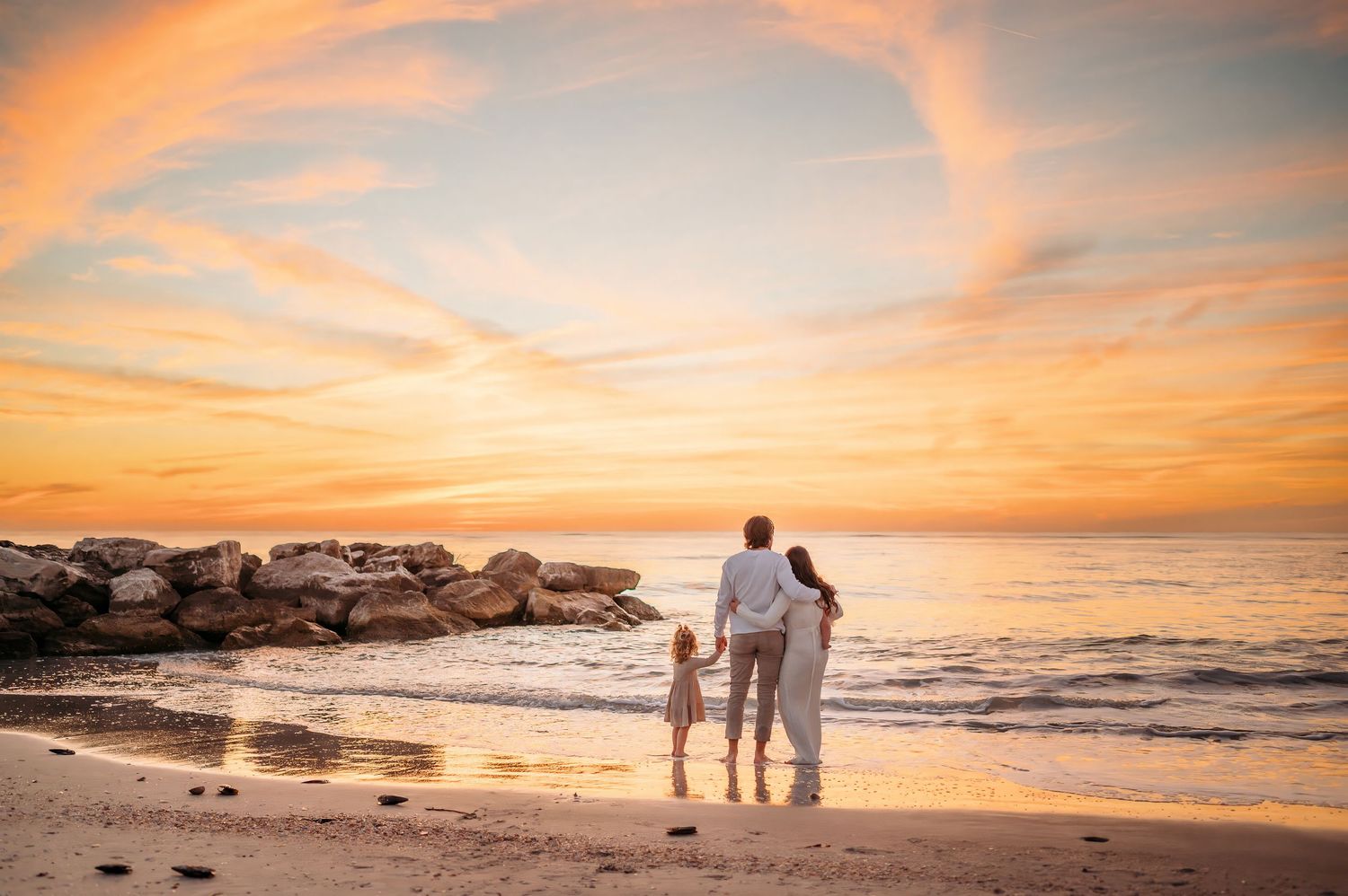 Panoramic beach sunset with family silhouettes and orange sky.