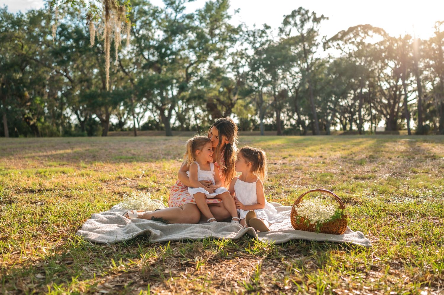 Mom and daughters enjoying an intimate sunset picnic on a grassy field during golden hour.
