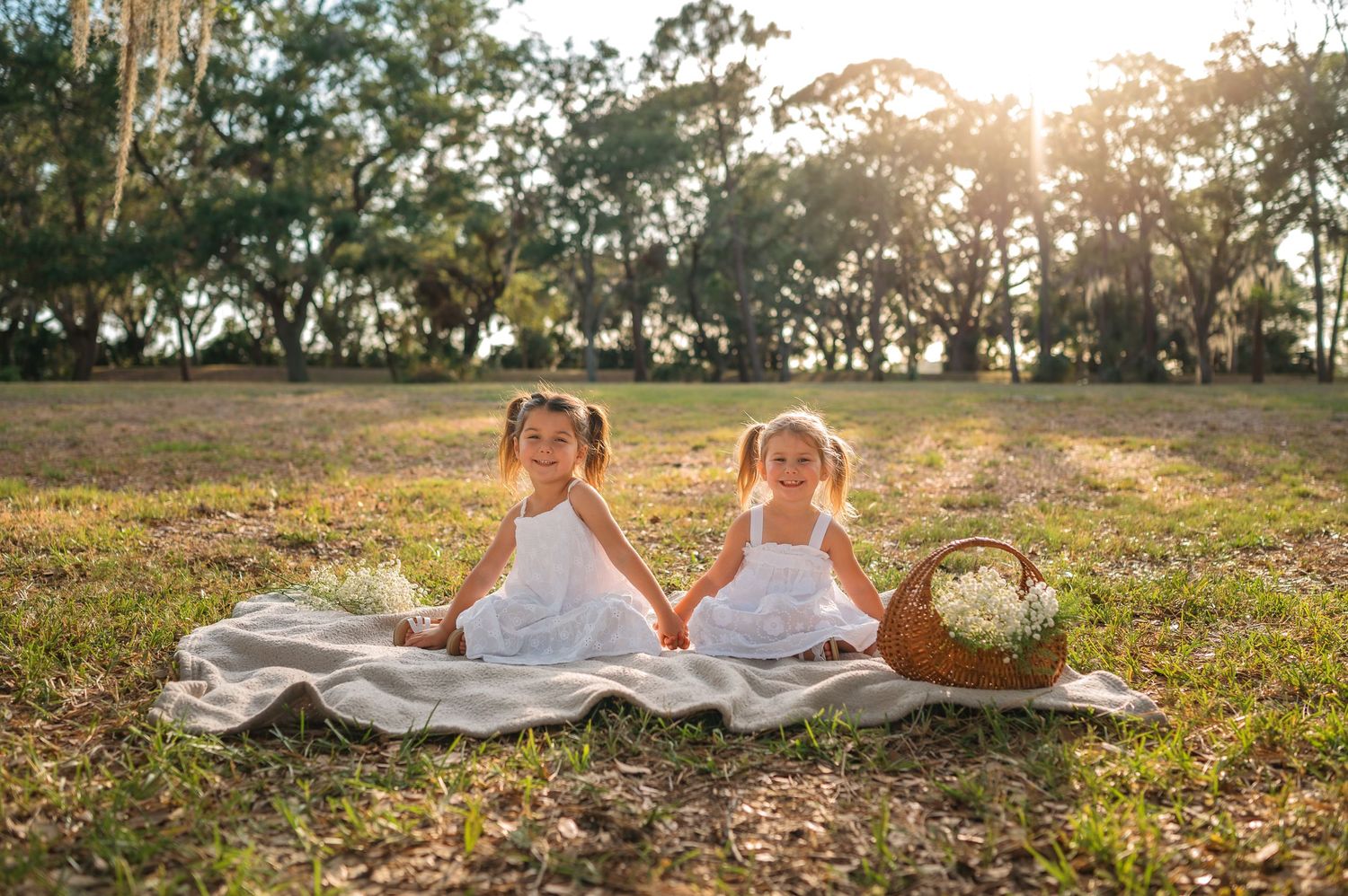 Dreamy outdoor photoshoot on blanket during golden hour with trees in background.