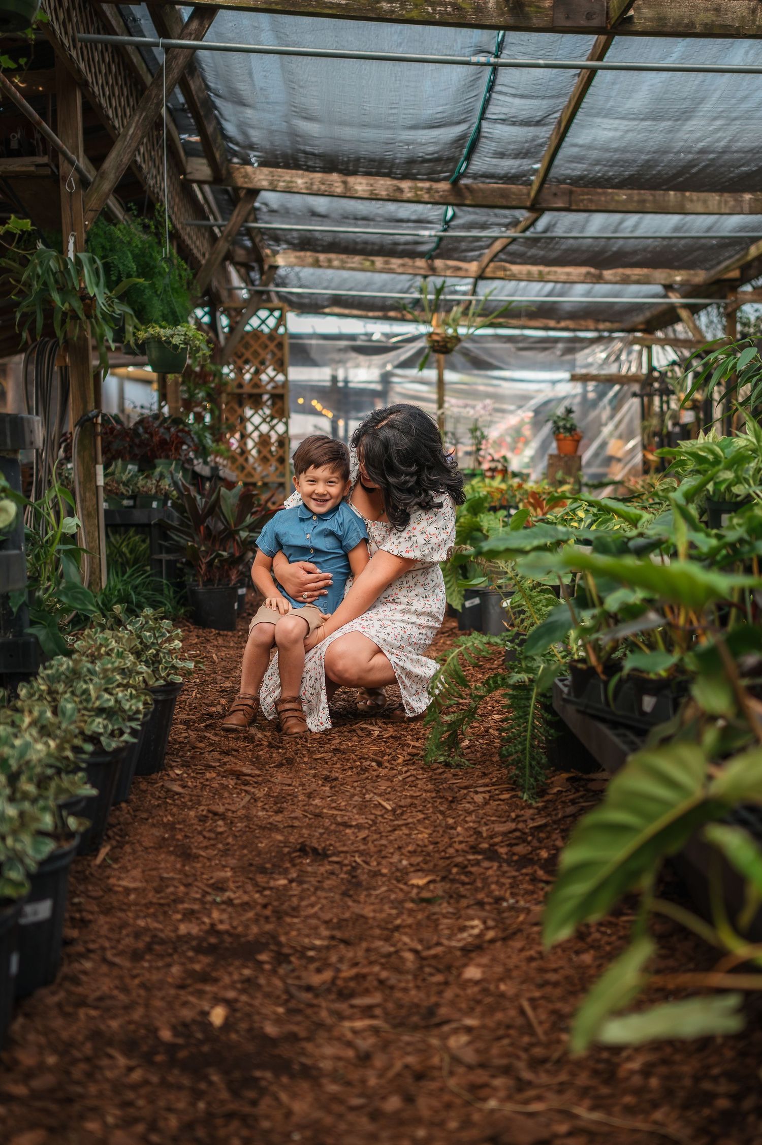 Natural light streams through a greenhouse roof while family interacts on mulch covered ground.