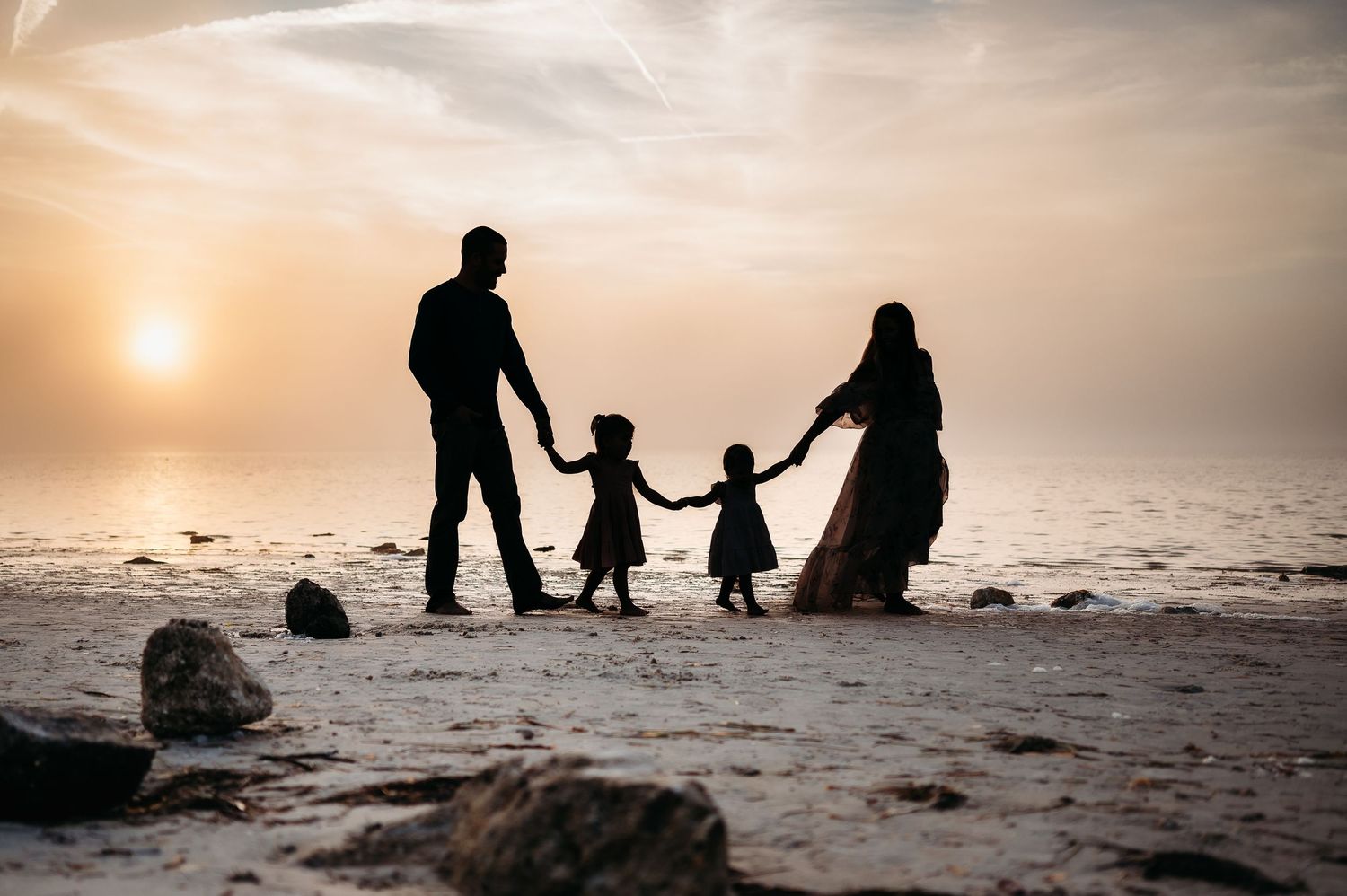 Silhouettes of family walking on beach at sunset creating dramatic shadows.