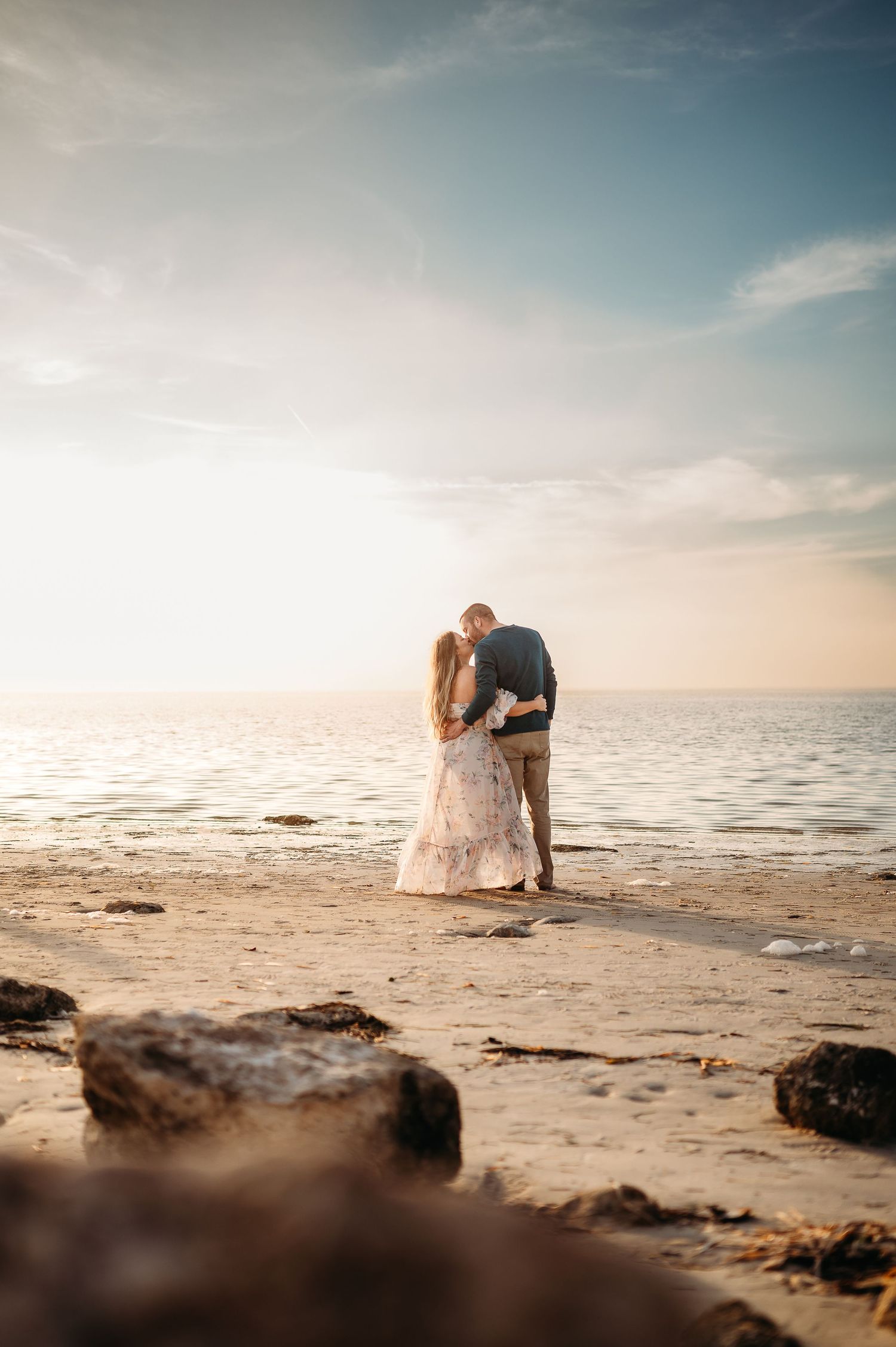 Romantic beach photoshoot with soft sunset lighting and ocean waves in background.