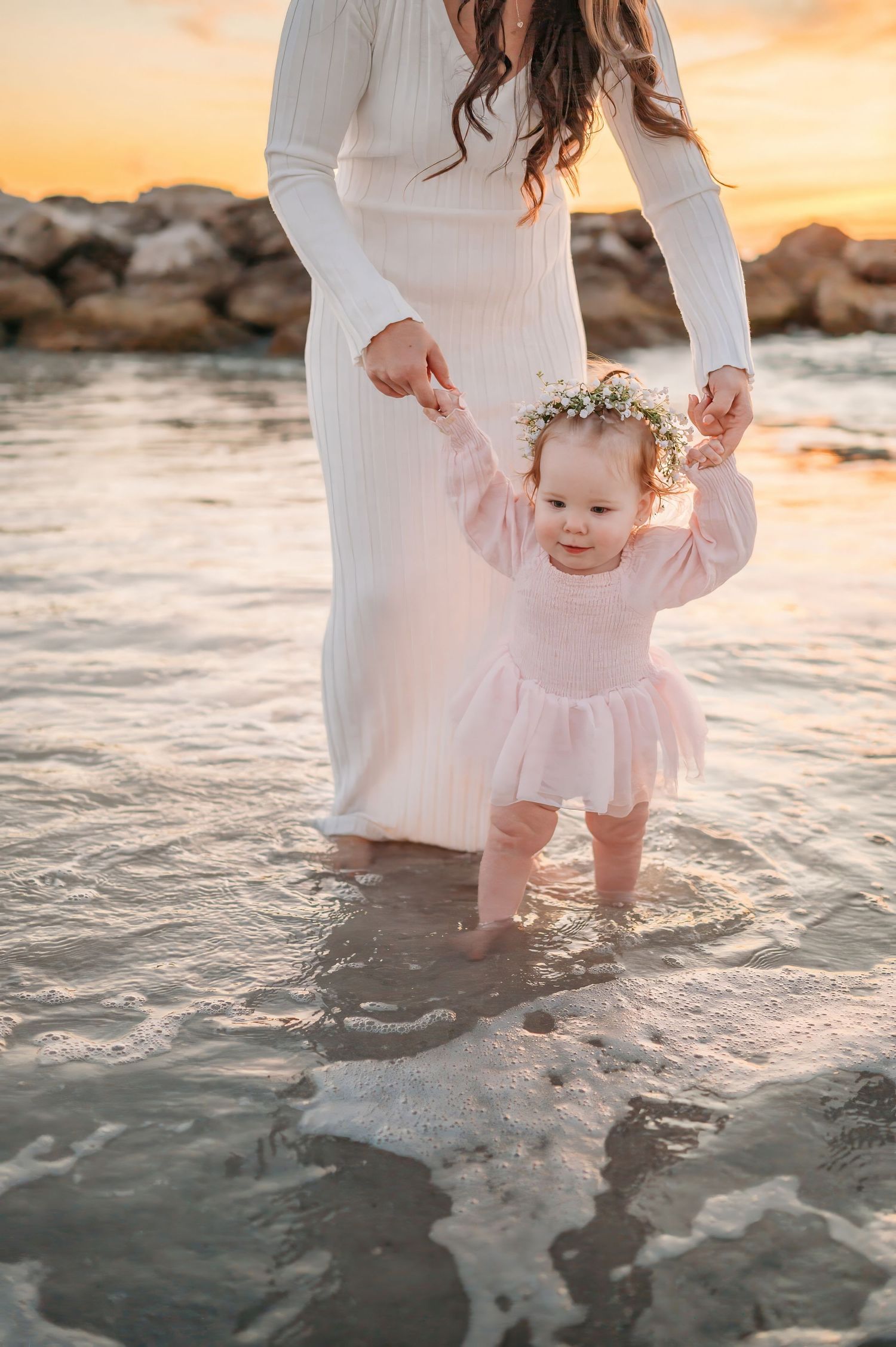 Gentle moment at the beach with white dress and pink outfit in shallow water at sunset.