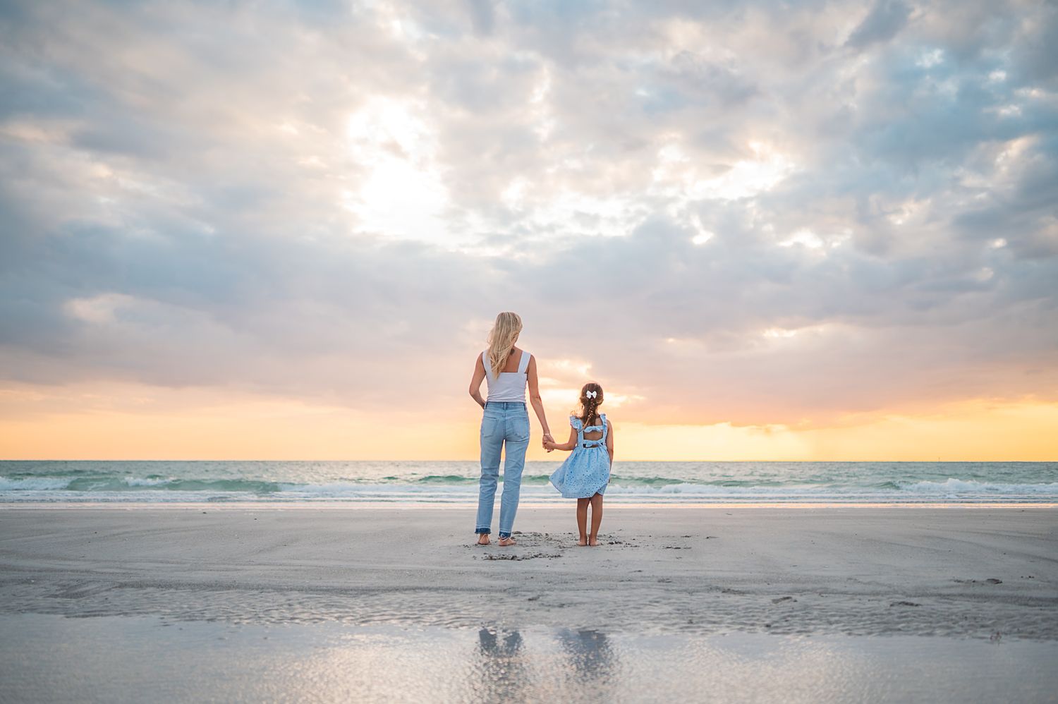 Family walking together along a sandy beach at sunset with dramatic clouds in the sky.