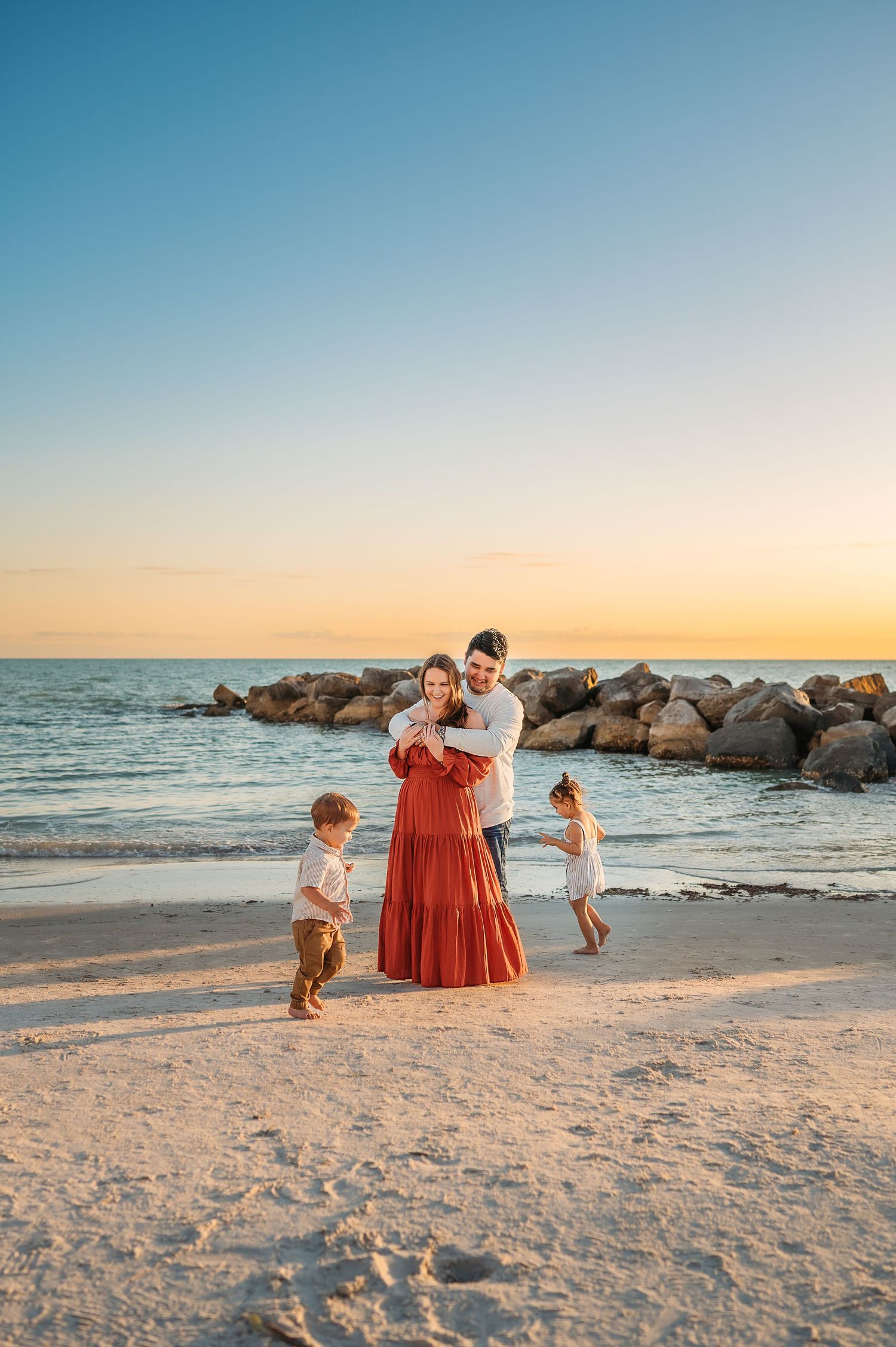 A family enjoys a sunset moment on a beach with rocky outcrops during golden hour.