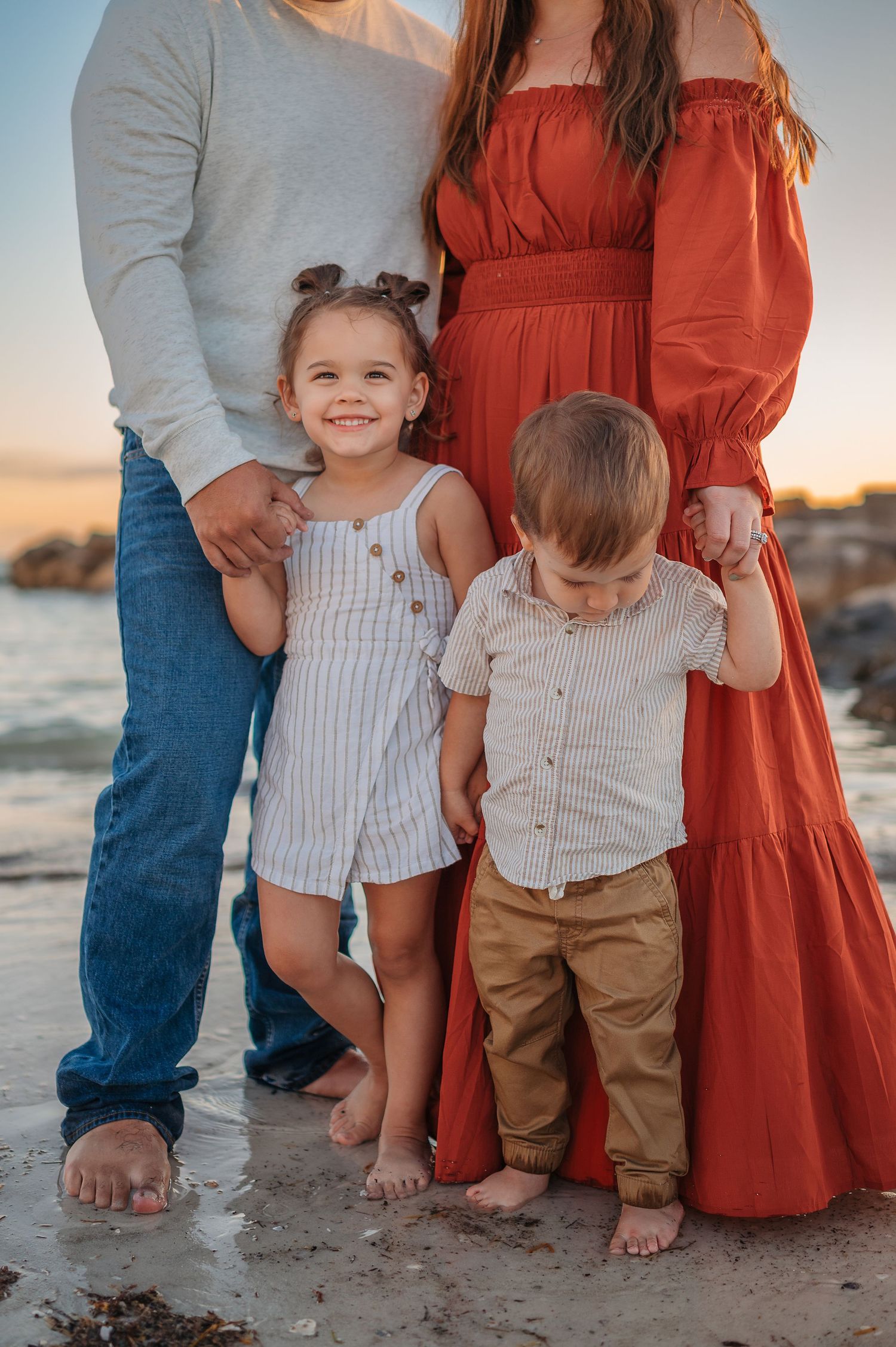 Close-up detail view of family members' standing together on sandy beach at sunset.