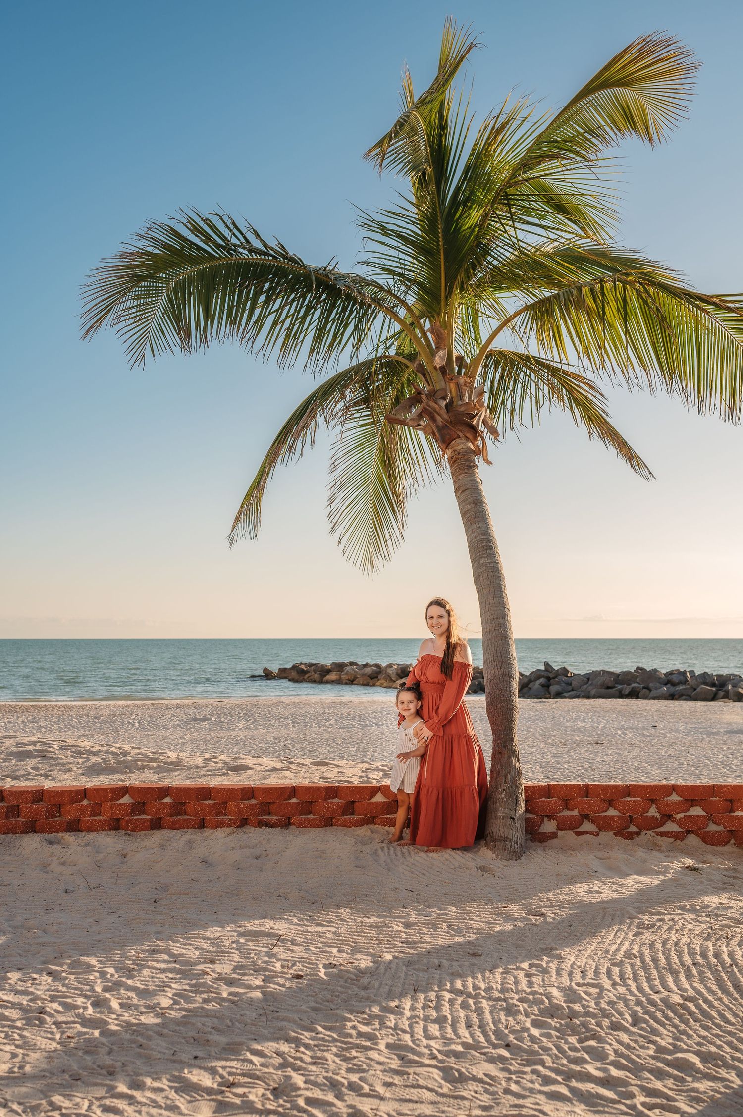 Tropical beach scene with palm trees and coral wall against white sand and blue ocean.