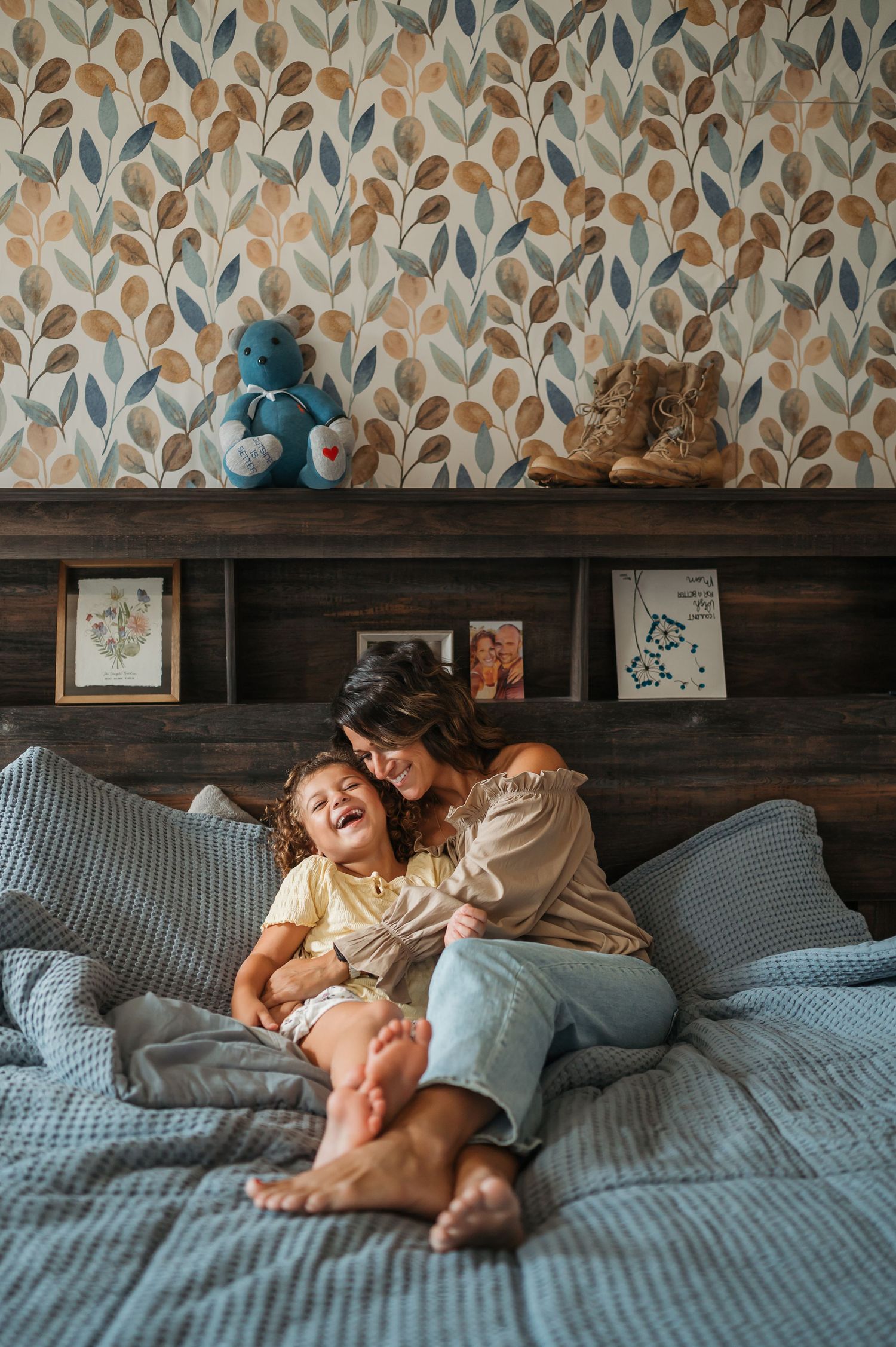 Relaxing scene on a bed with floral wallpaper backdrop and gray pillows.