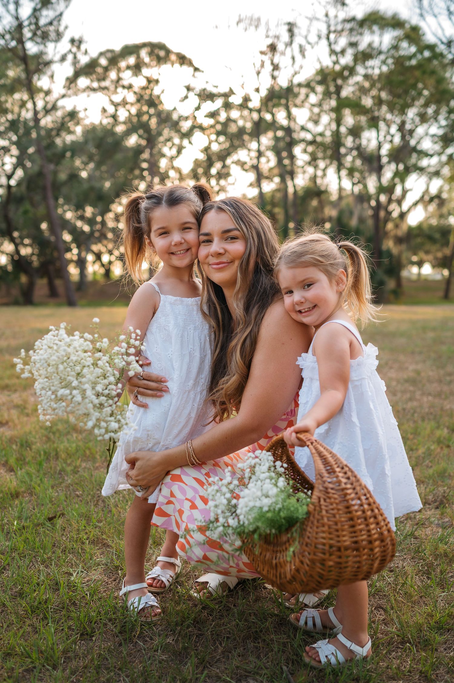Loving family portrait session in field with white dresses and wildflower bouquet at sunset.