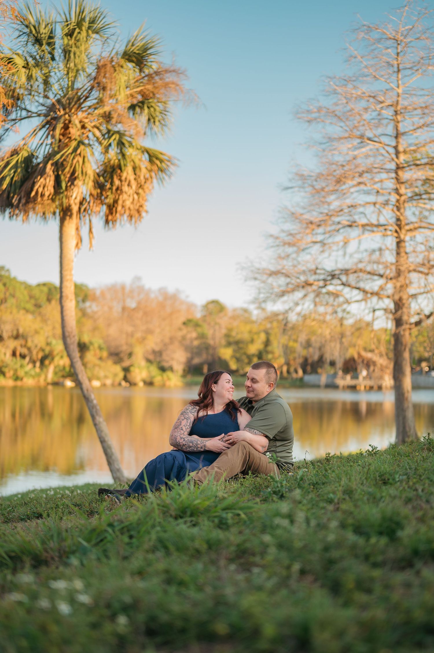 Couple relaxing by lakeside under palm trees during golden hour.