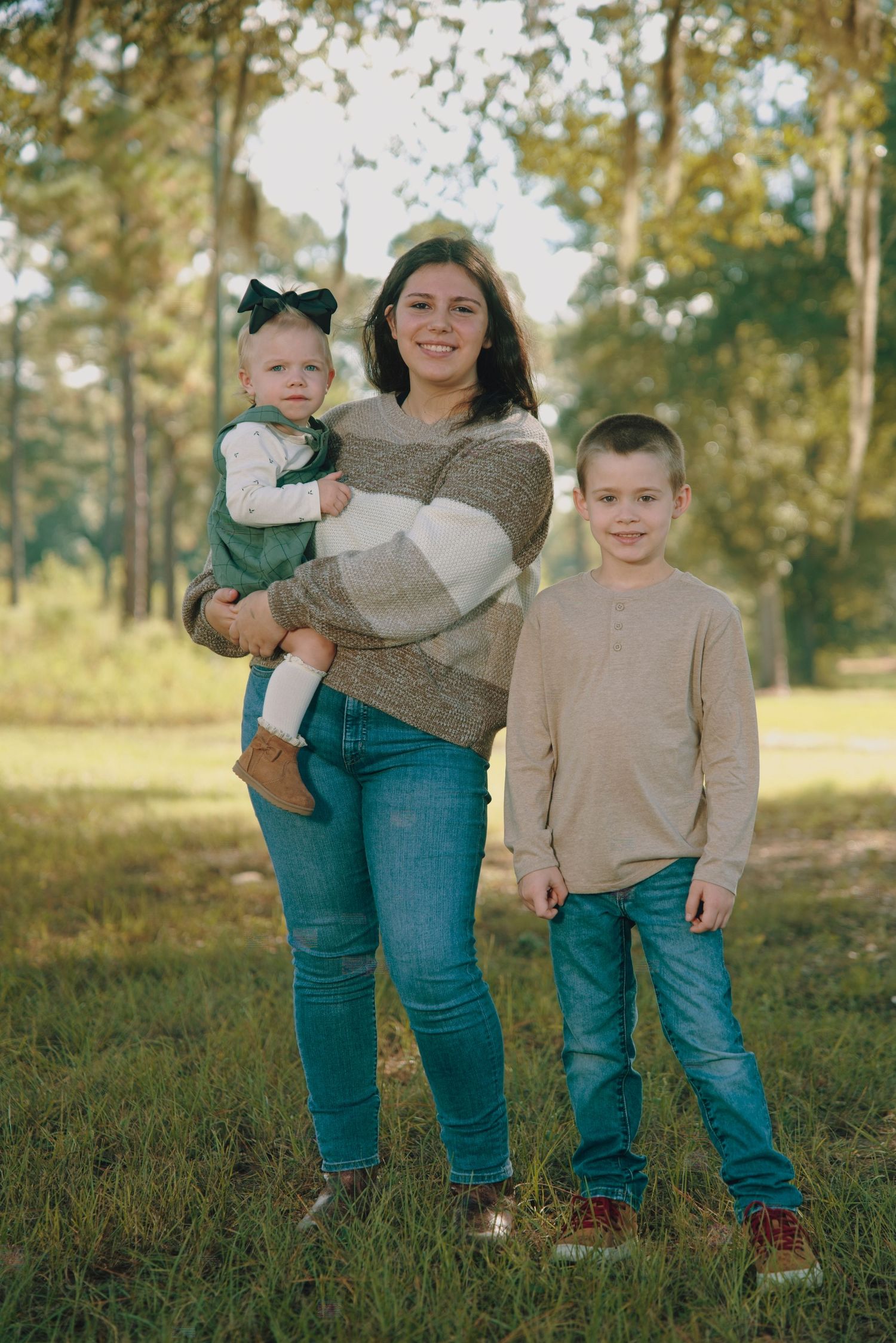 A family wearing coordinated outfits in beige and teal poses together in a grassy outdoor setting during golden hour.