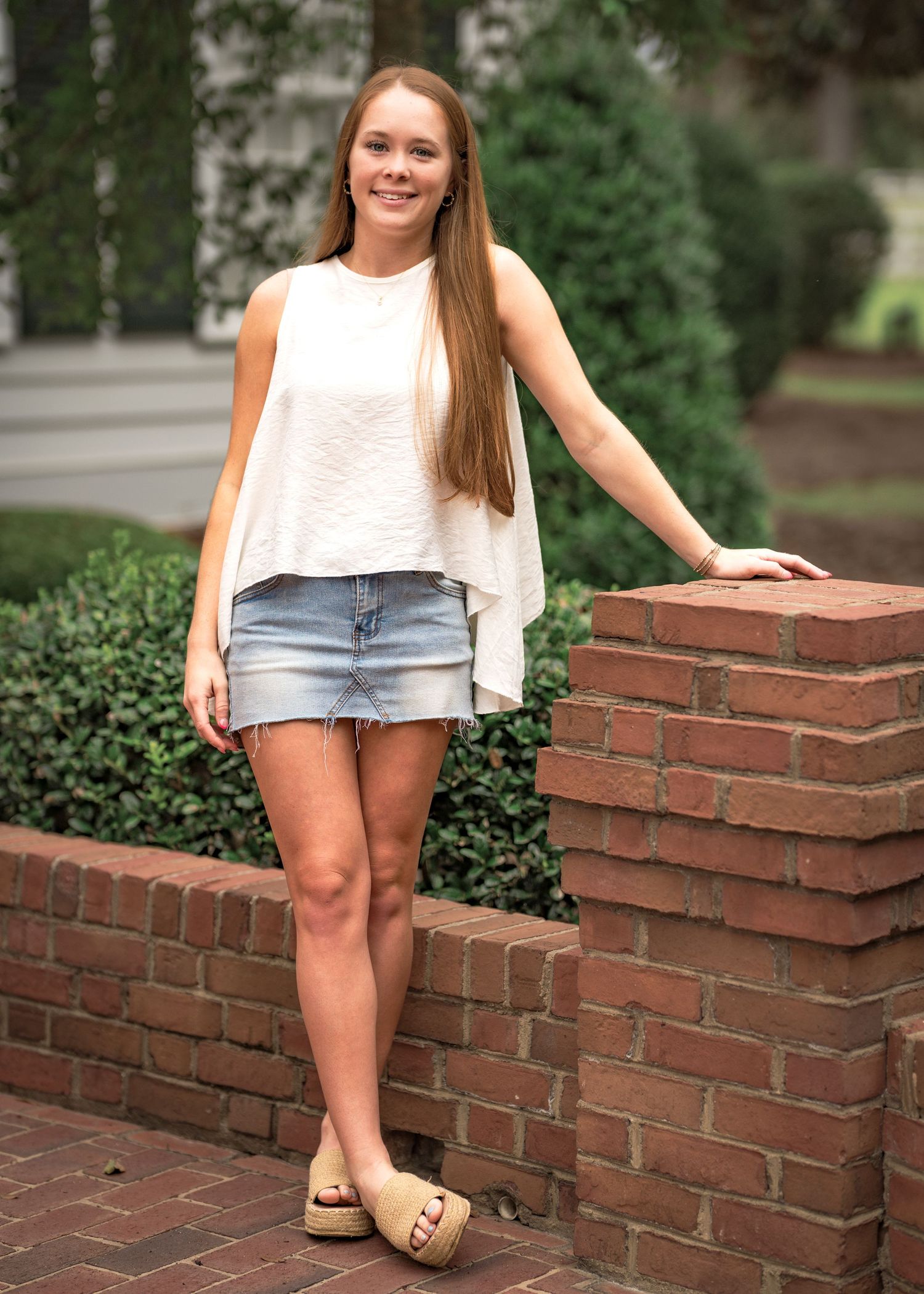Person sitting on brick ledge wearing denim shorts and white top in garden setting.