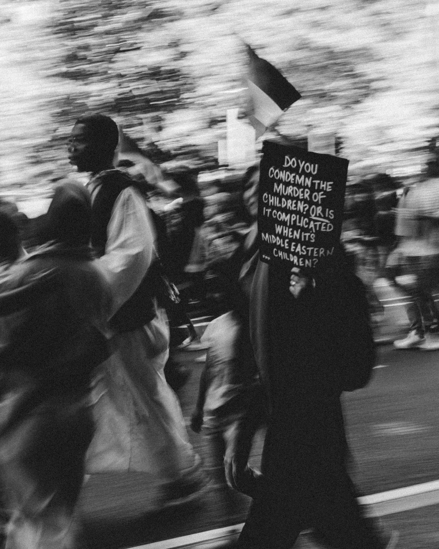 Protester carries sign reading anti-war message while marching in blurred crowd in black and white.