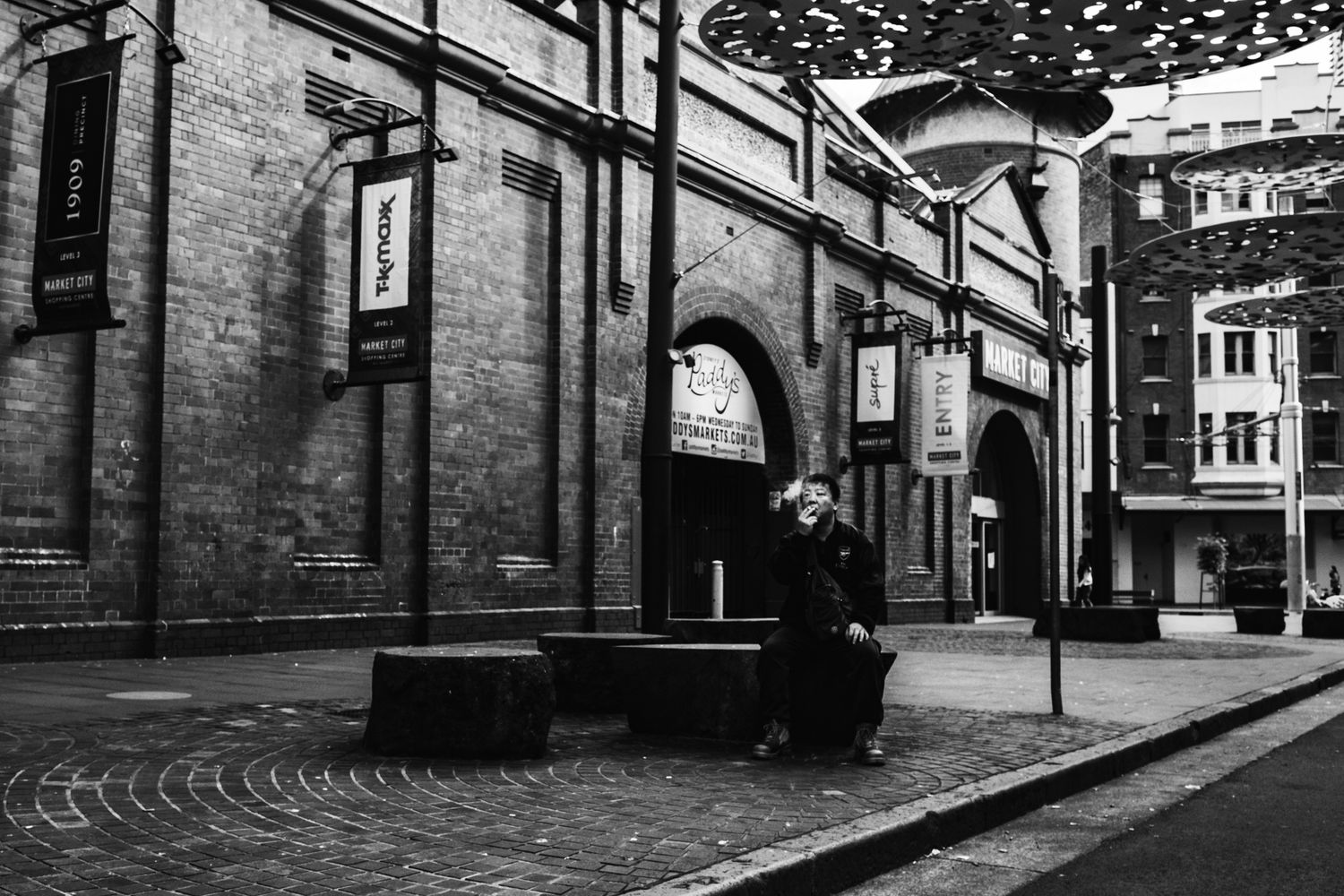Solitary person sits on bench outside historic brick building on empty cobblestone street at night.