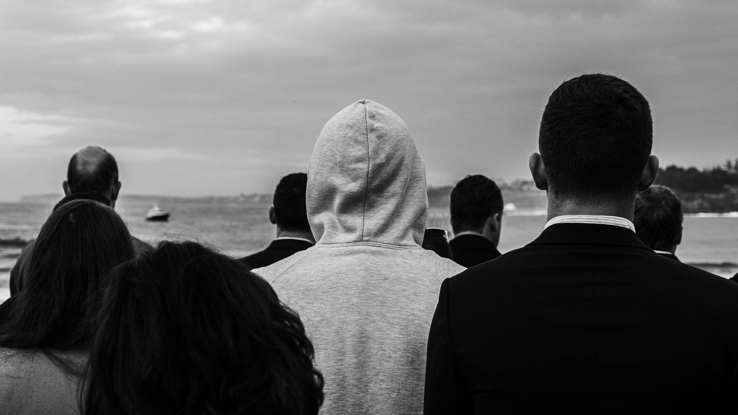 Group of people seen from behind gazing at the ocean horizon in a black and white photograph.