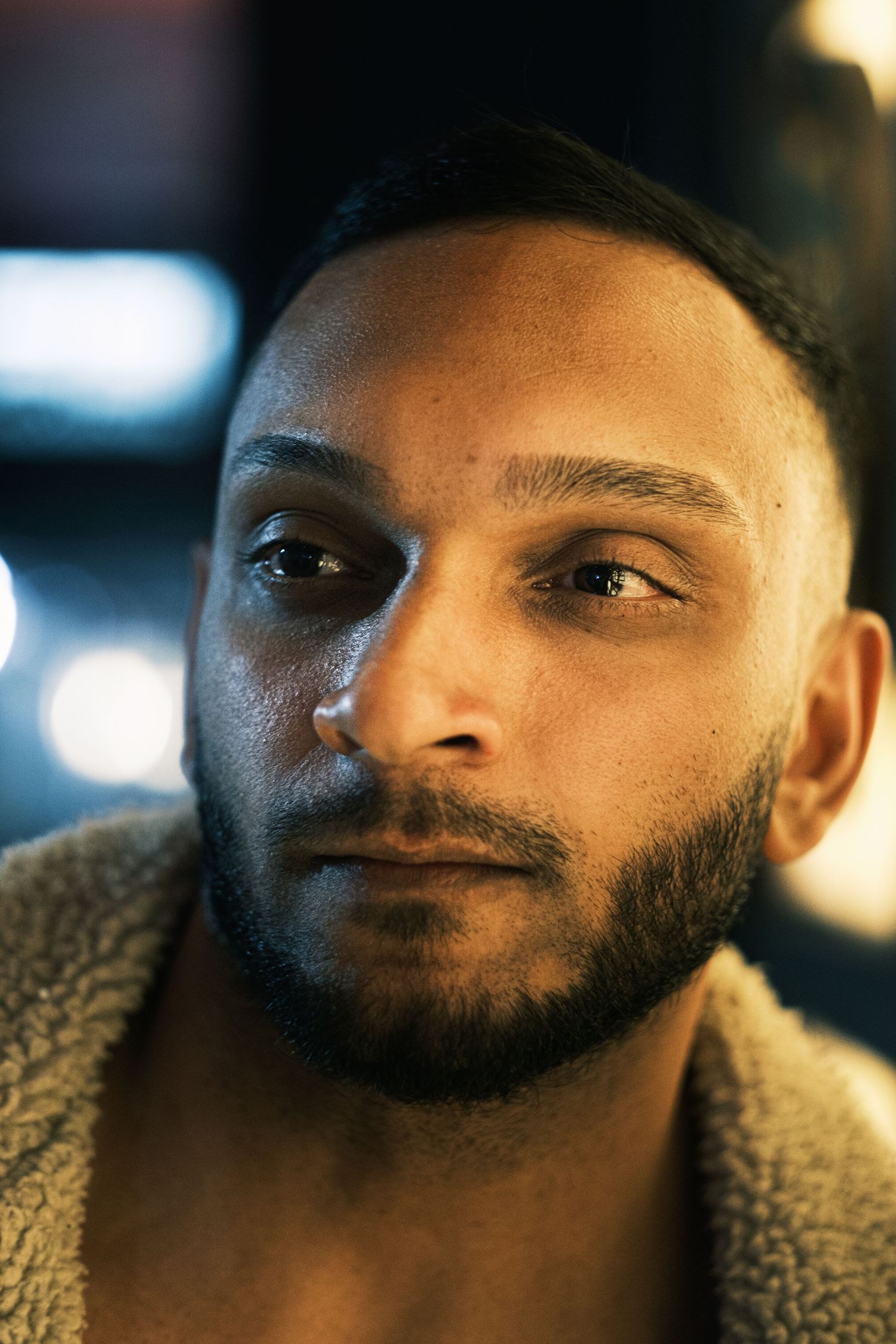 Dramatic close-up portrait of a young bearded man with intense gaze in dark atmospheric lighting.