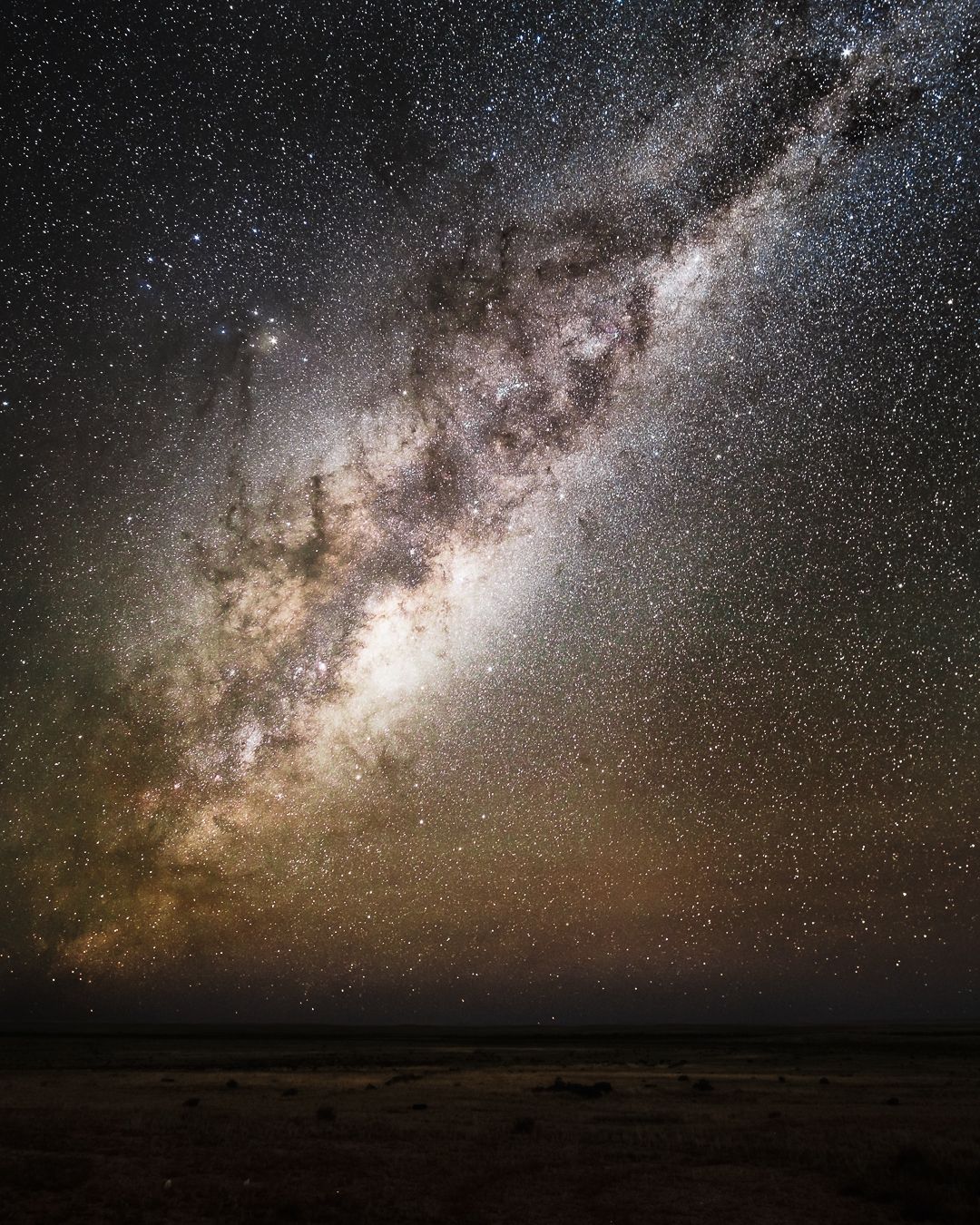Spectacular Milky Way galaxy stretches across a dark clear night sky above a flat desert horizon.