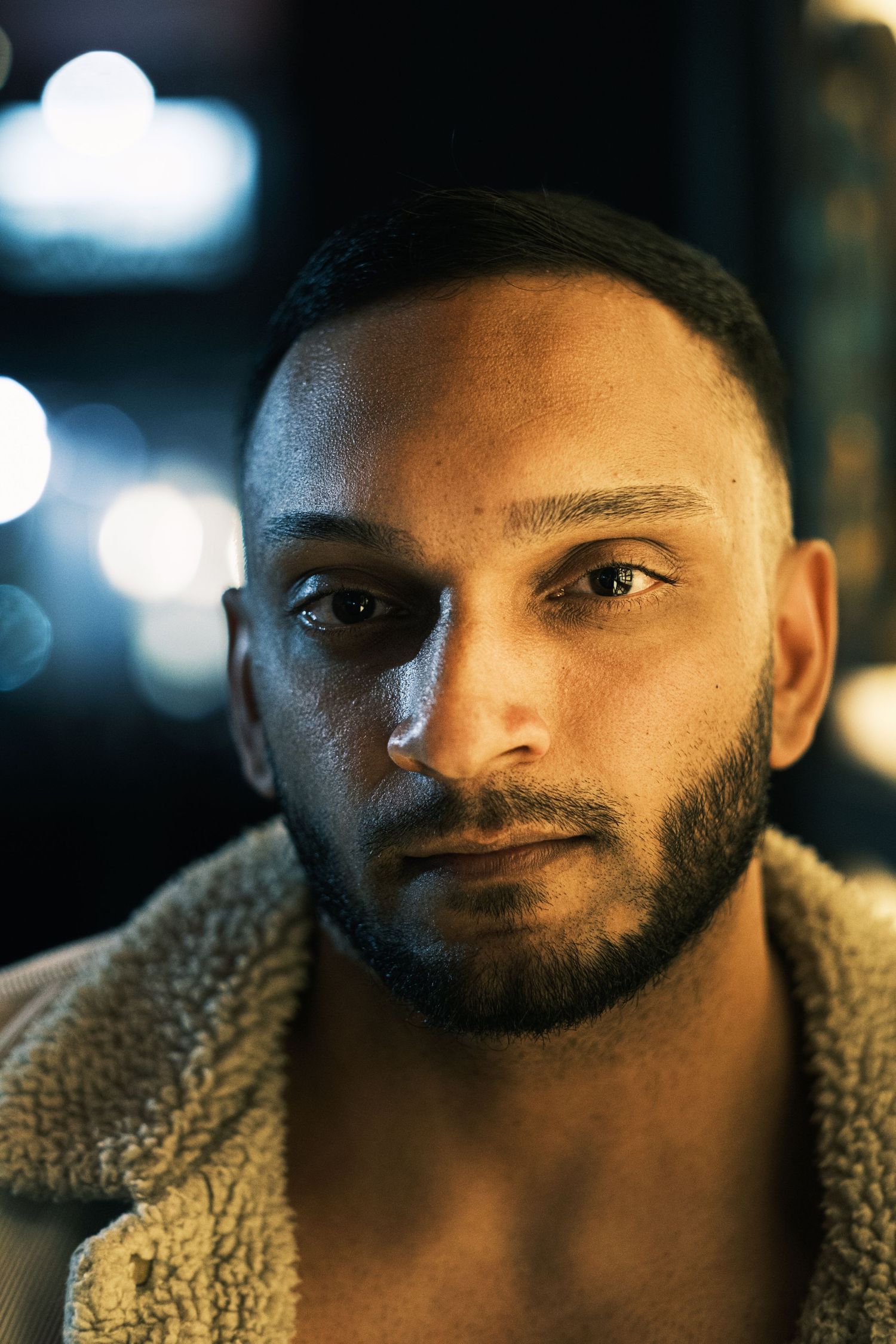 Close-up portrait of a bearded man with short hair wearing a sherpa jacket in moody bokeh lighting.