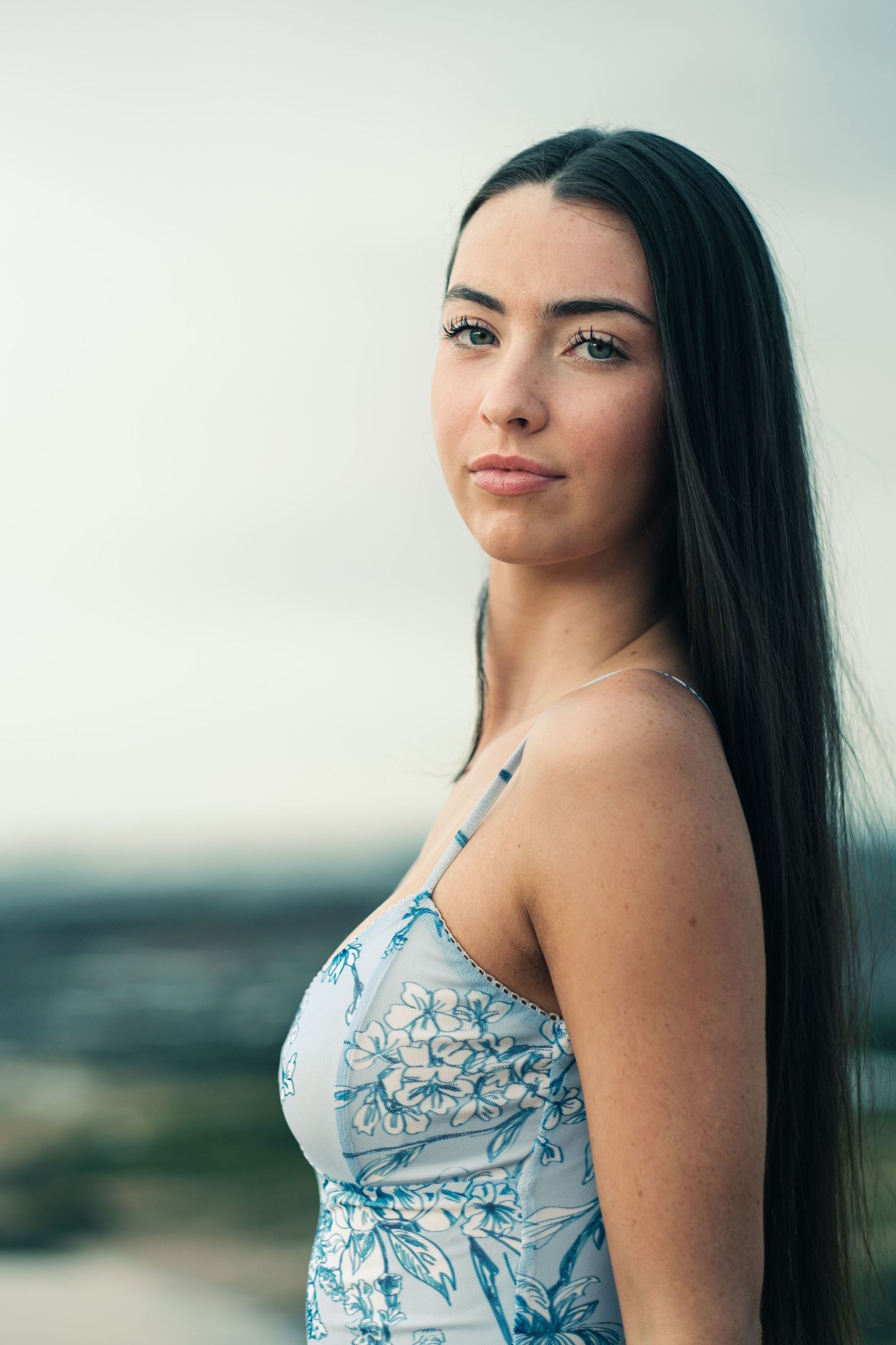 Portrait of a young woman with long dark hair wearing a blue floral dress outdoors.