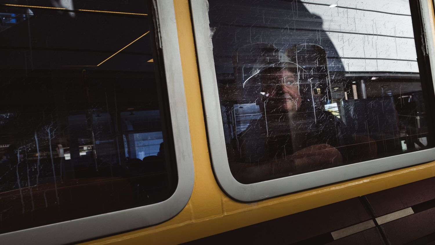 Contemplative person gazes through yellow public transit bus window in moody street photography.