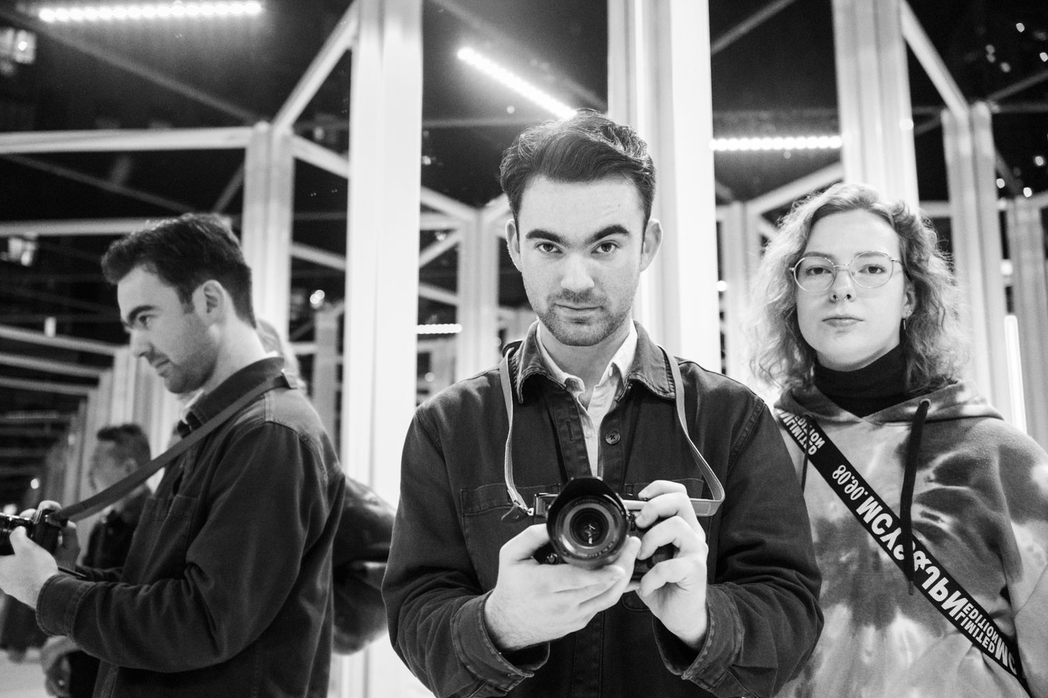 Black and white photo of photographer holding camera with two people in background.