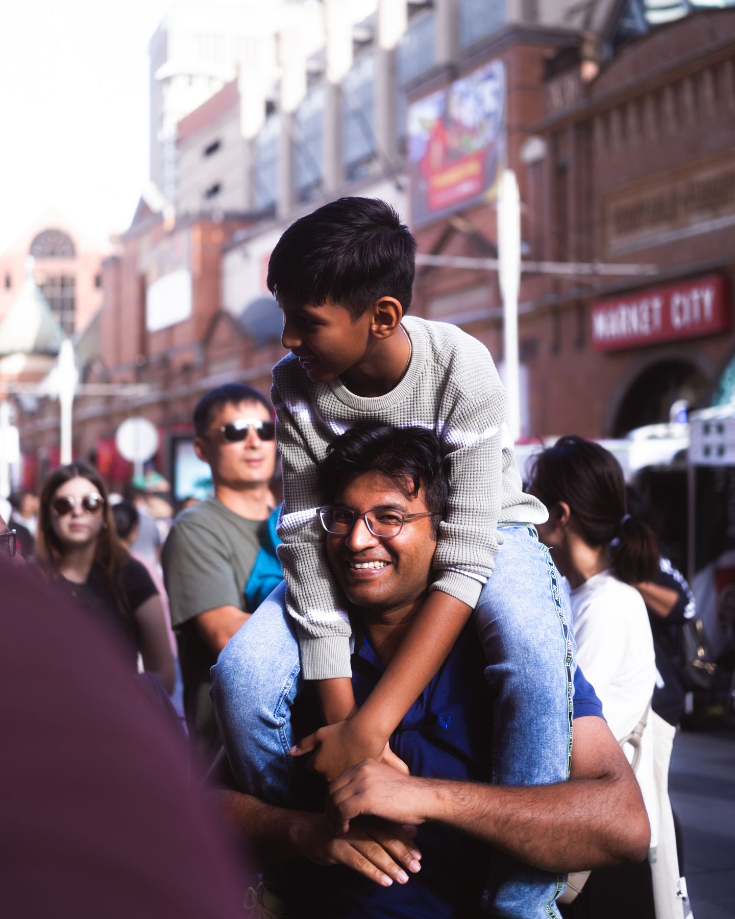 Smiling man carrying young boy on his shoulders on a busy urban street near Market City.