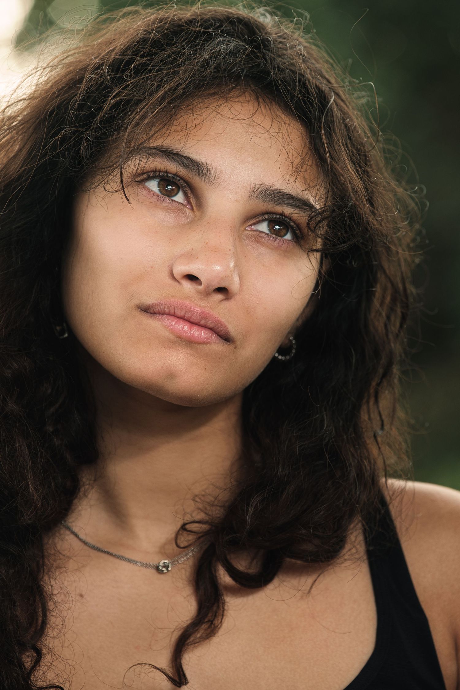 Young woman with curly dark hair and green eyes wearing a black top and choker necklace outdoors.