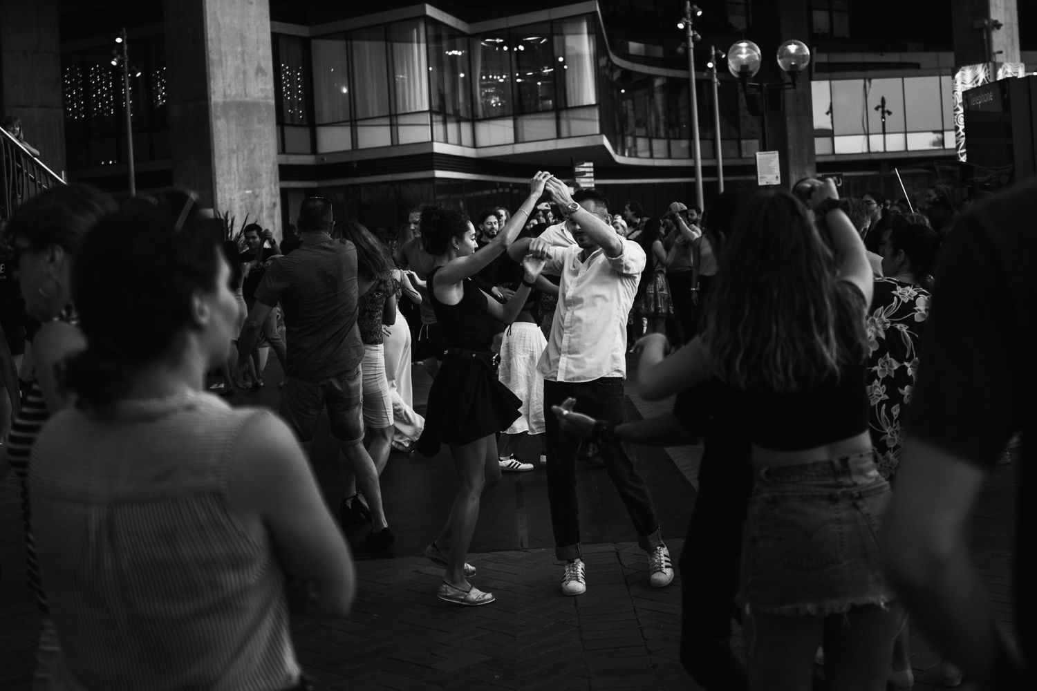 Crowd of people dancing outdoors at night in a busy urban street setting.