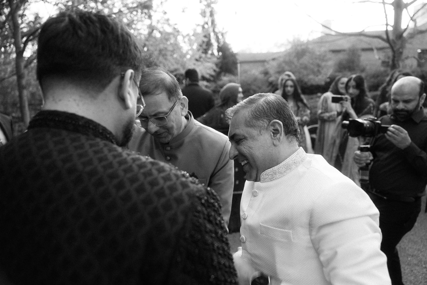Black and white photo of elegantly dressed guests socializing outdoors at a formal event or wedding.