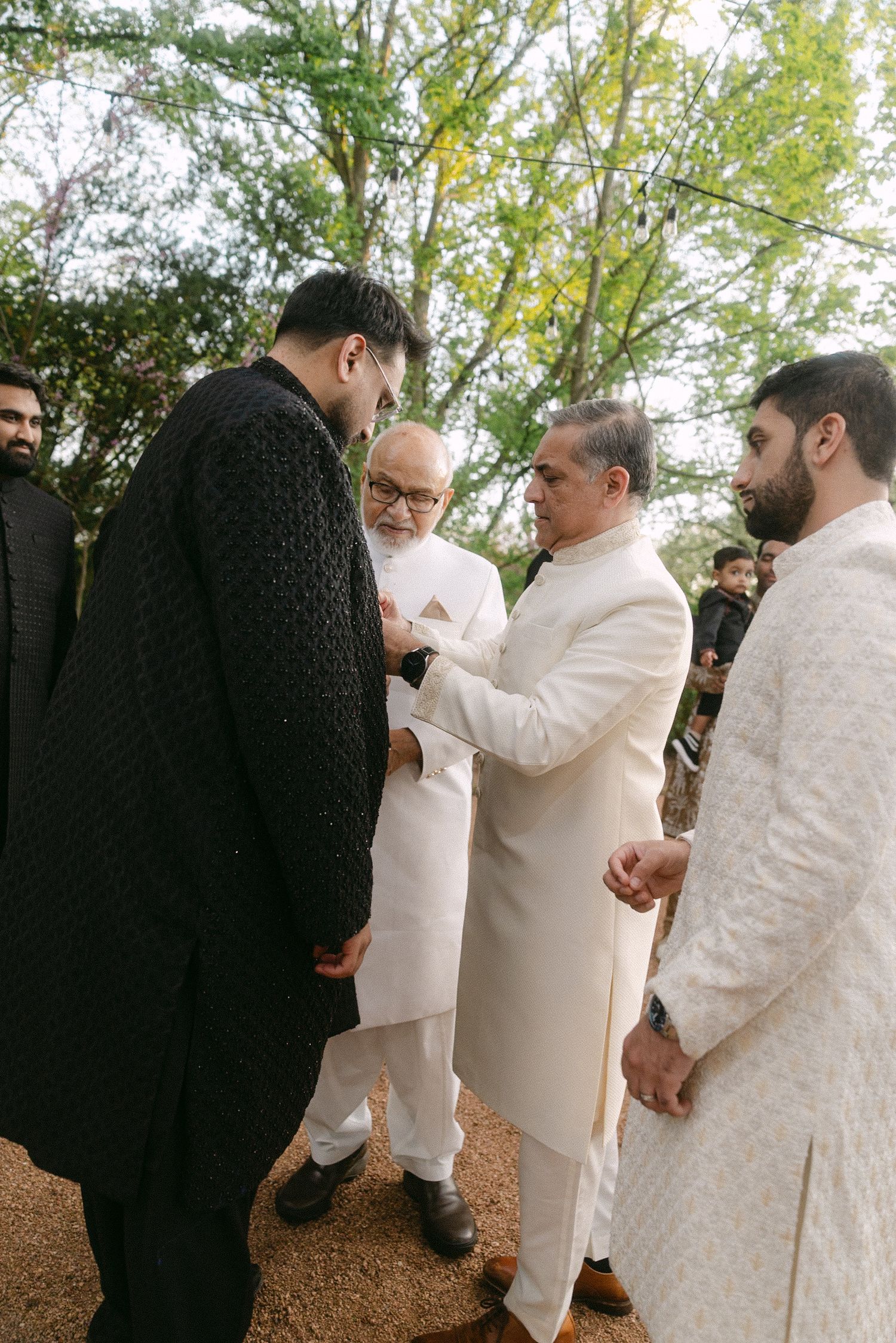 Men in traditional South Asian attire, including black and white sherwanis, gather outdoors at a formal cultural celebration.
