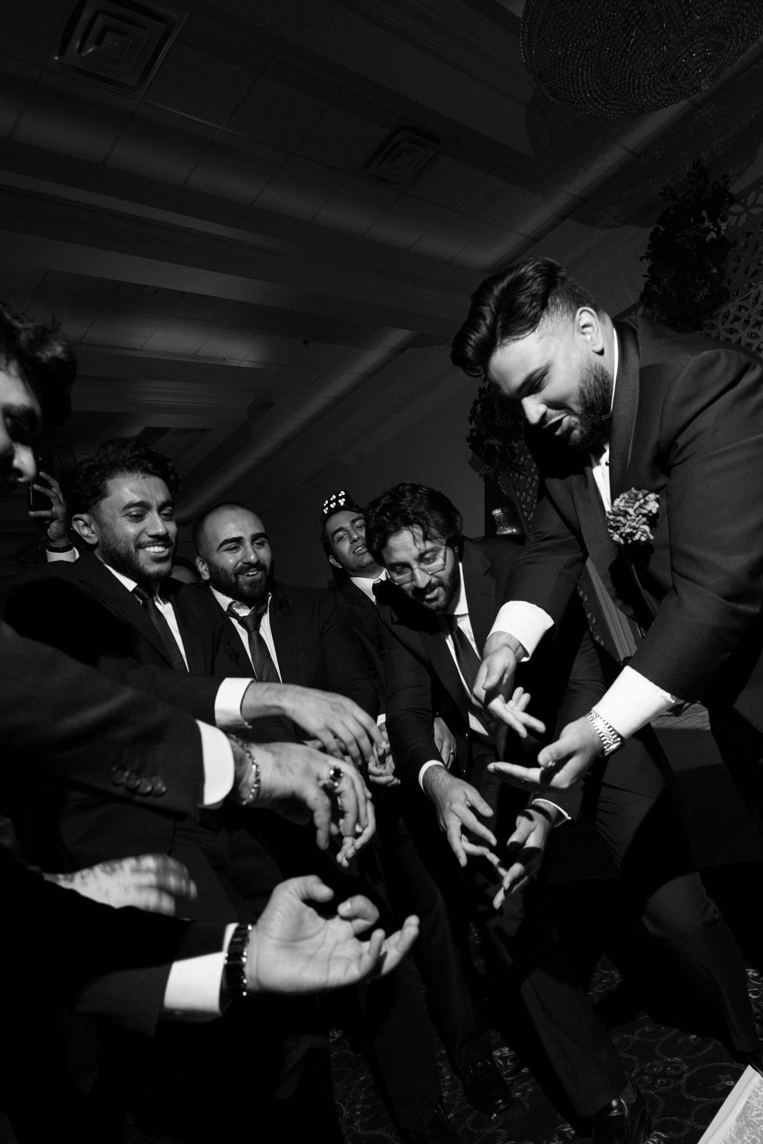 Black and white photo of groom in suit sharing a joyful moment with groomsmen at a wedding reception.