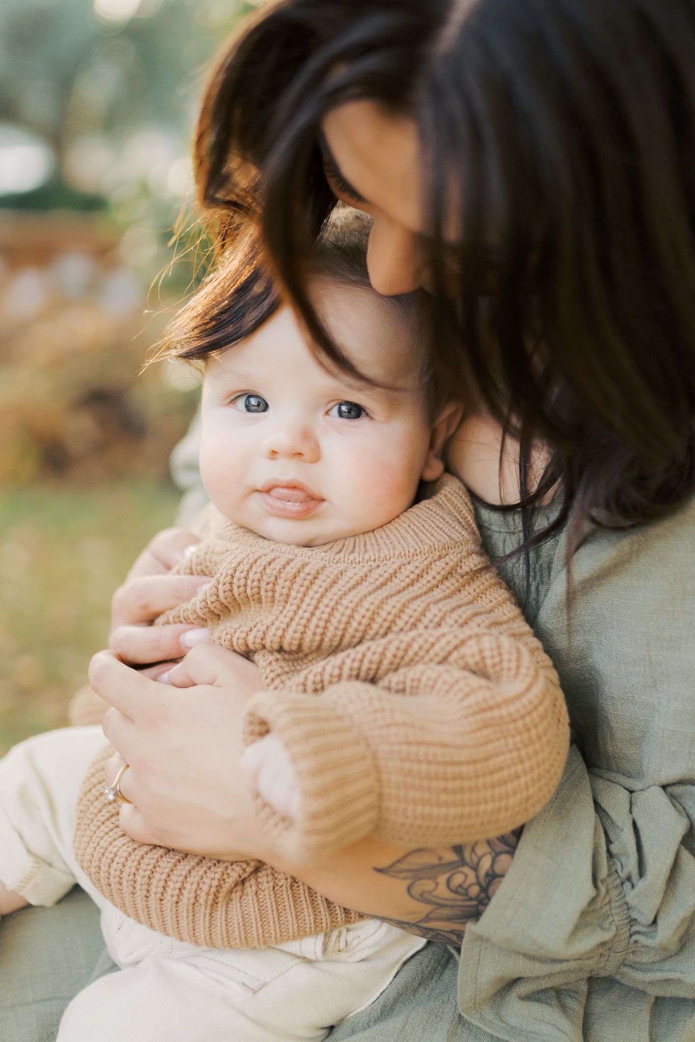 Baby boy dressed in a warm knitted jumper looking up at the camera while being snuggled close by his mother