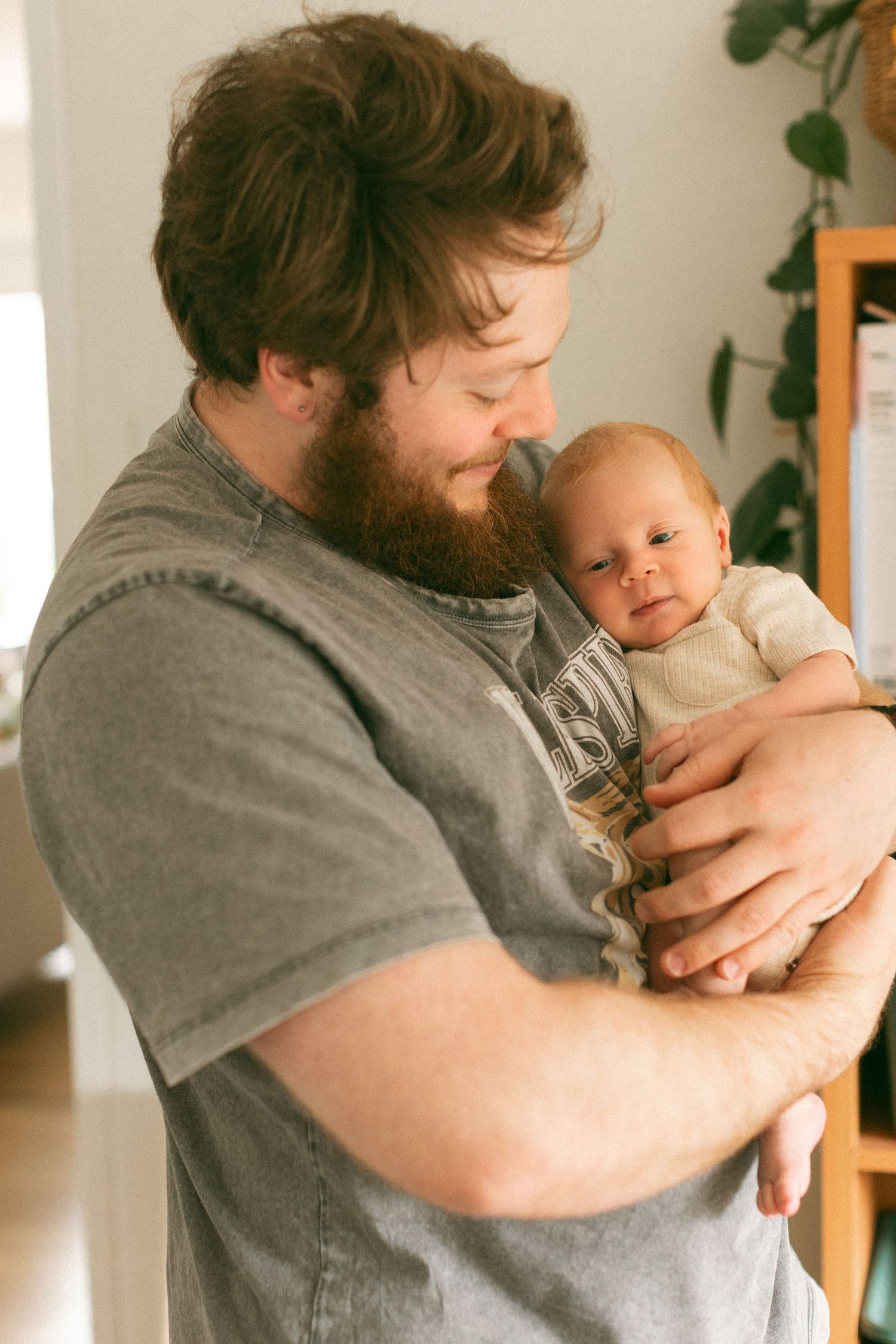Father holding newborn baby boy, looking down and smiling at him.