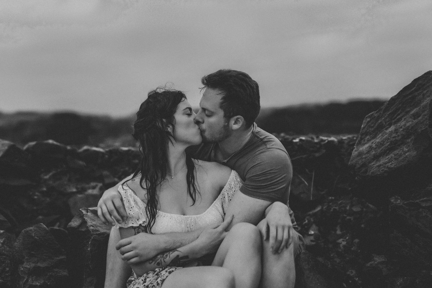 Couple kissing and embracing on a rocky beach in the rain.