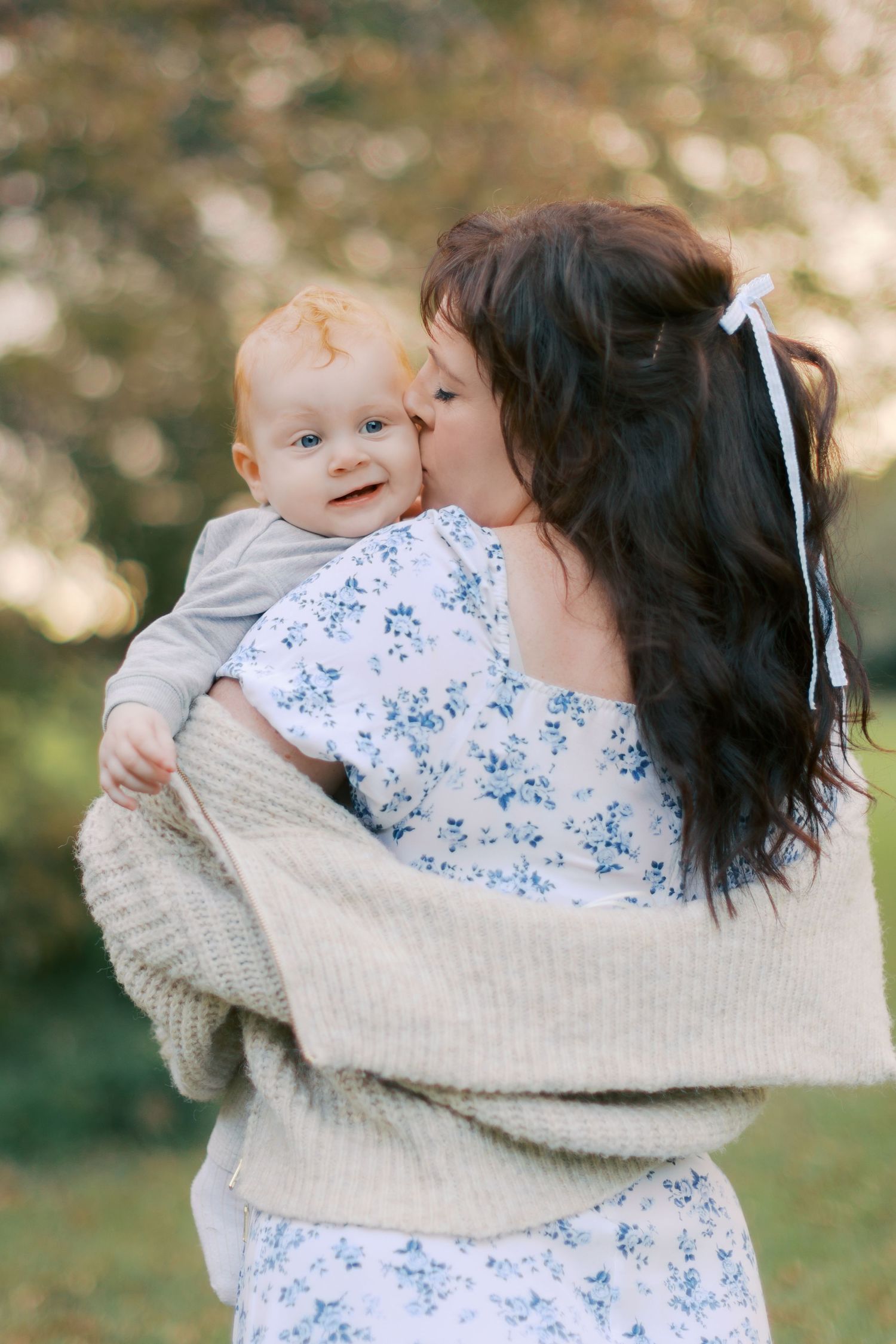Mother holding baby boy and giving him a kiss while he looks over her shoulder at the camera.