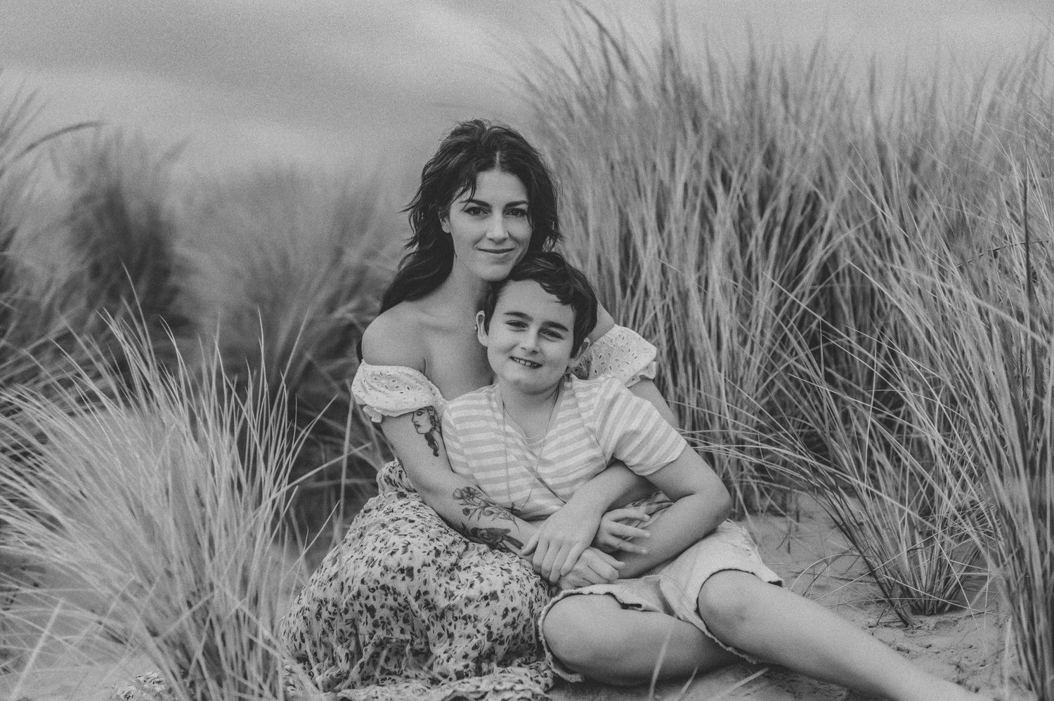 Mother and son smiling at camera on the beach.