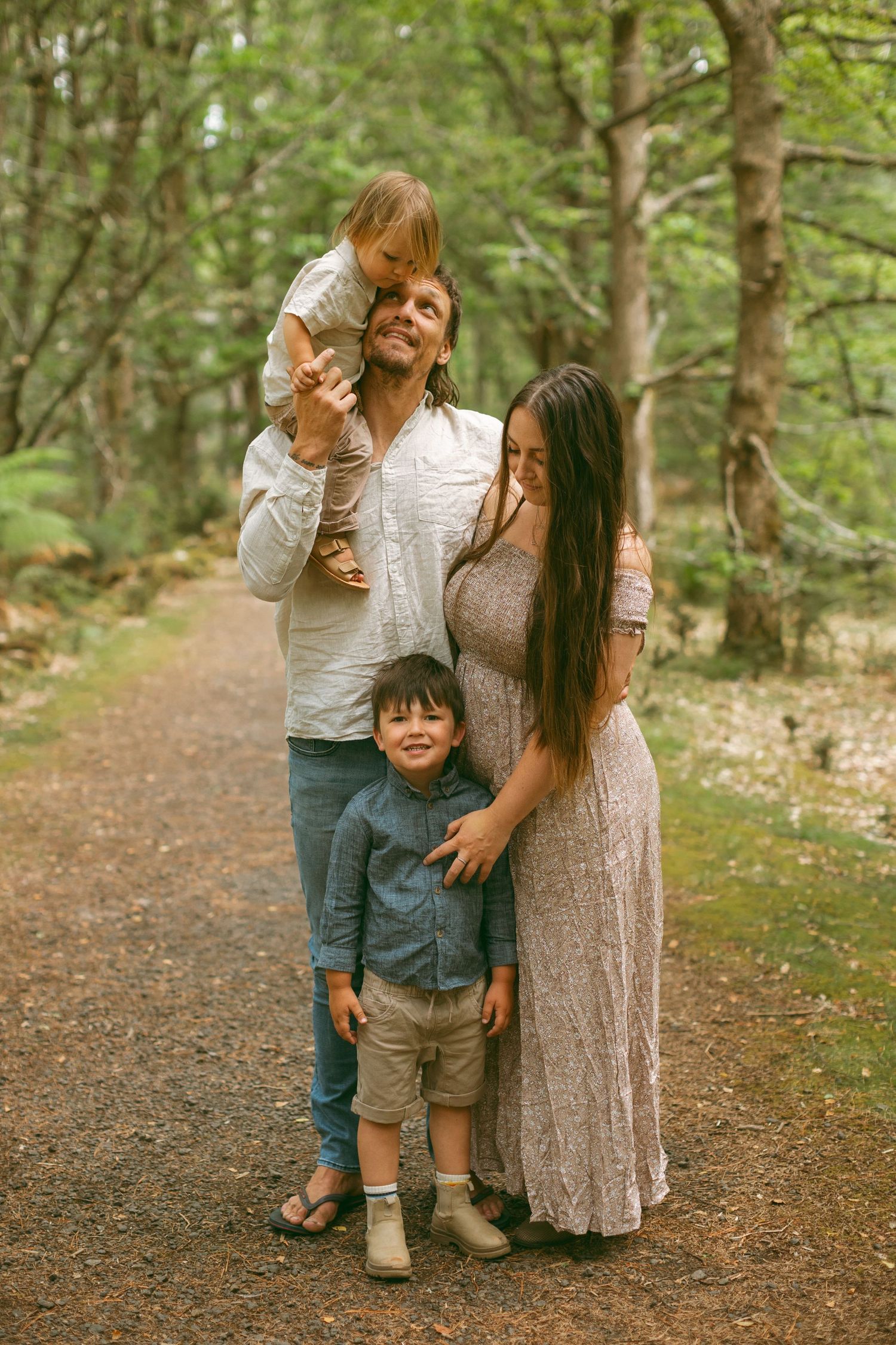 Family of four standing together in the forest, one boy on Dad's shoulders and the other boy standing next to Mum.
