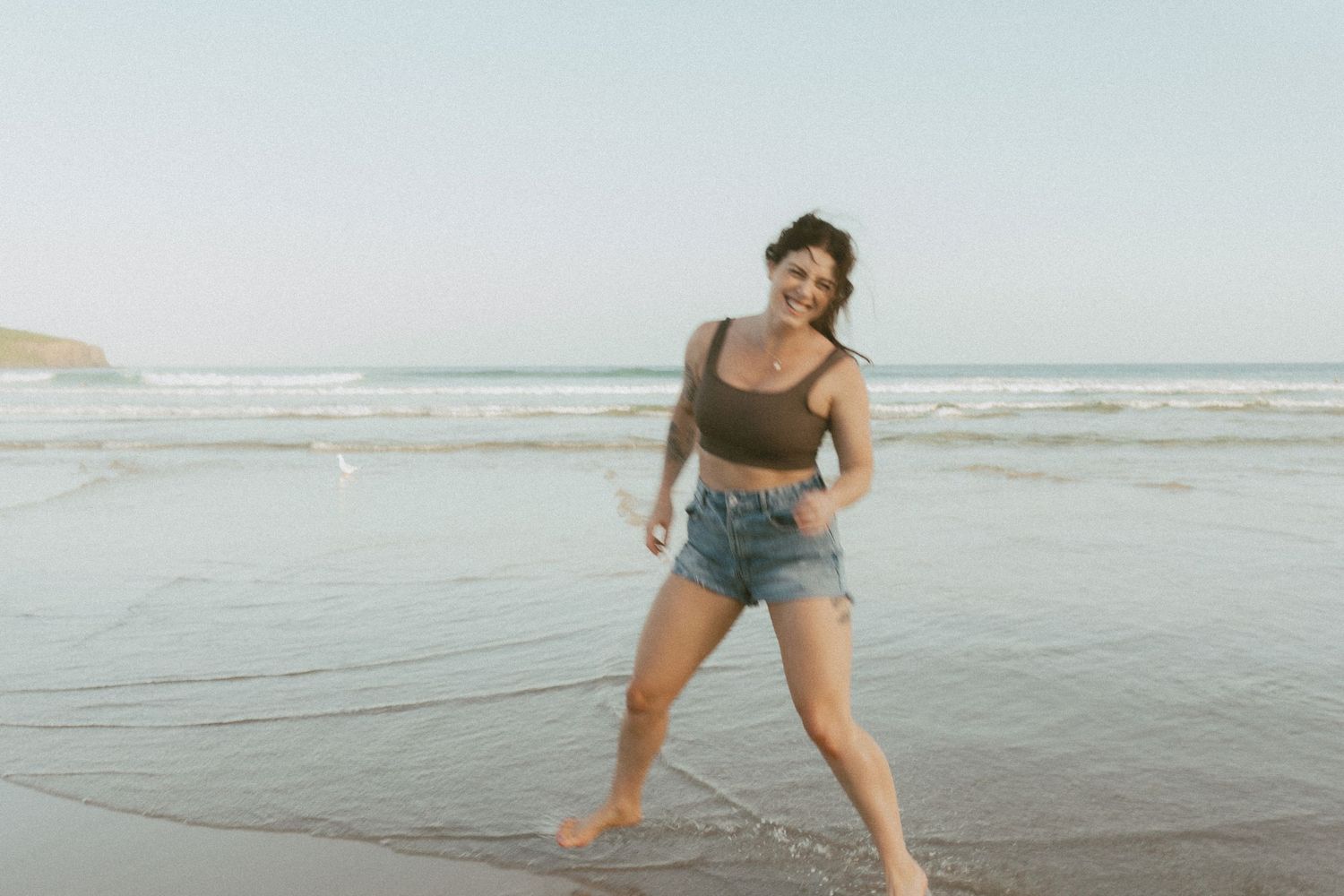 Woman smiling at camera while playing in shallow water at the beach.
