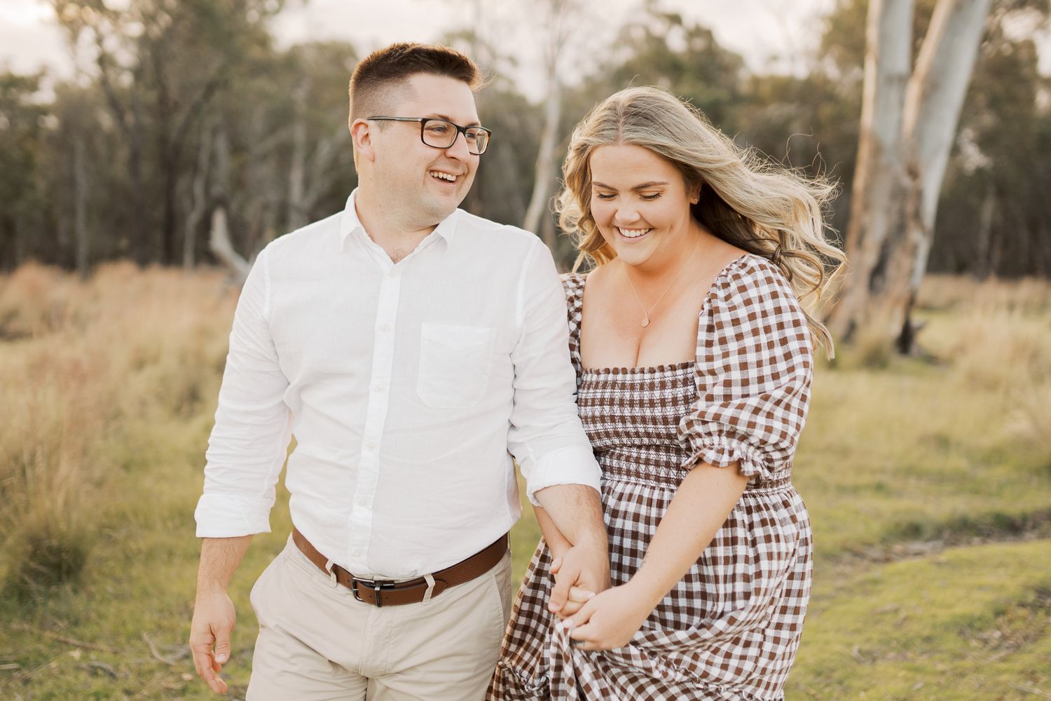 Engaged couple smiling while walking through field, Wollongong